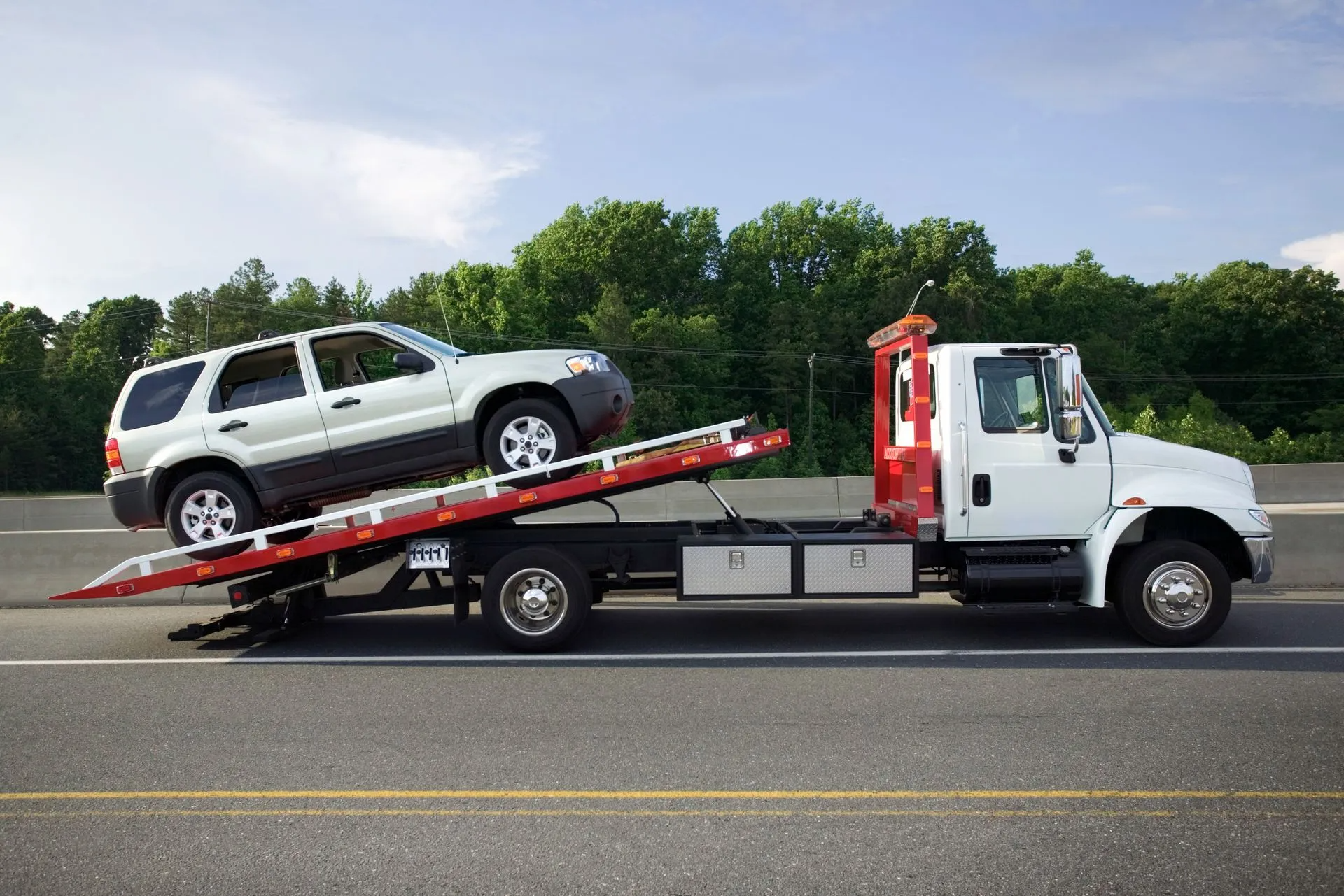 White SUV being towed on a flatbed tow truck on a highway.