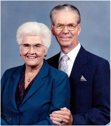 Elderly couple in formal attire smiles at camera, studio background.
