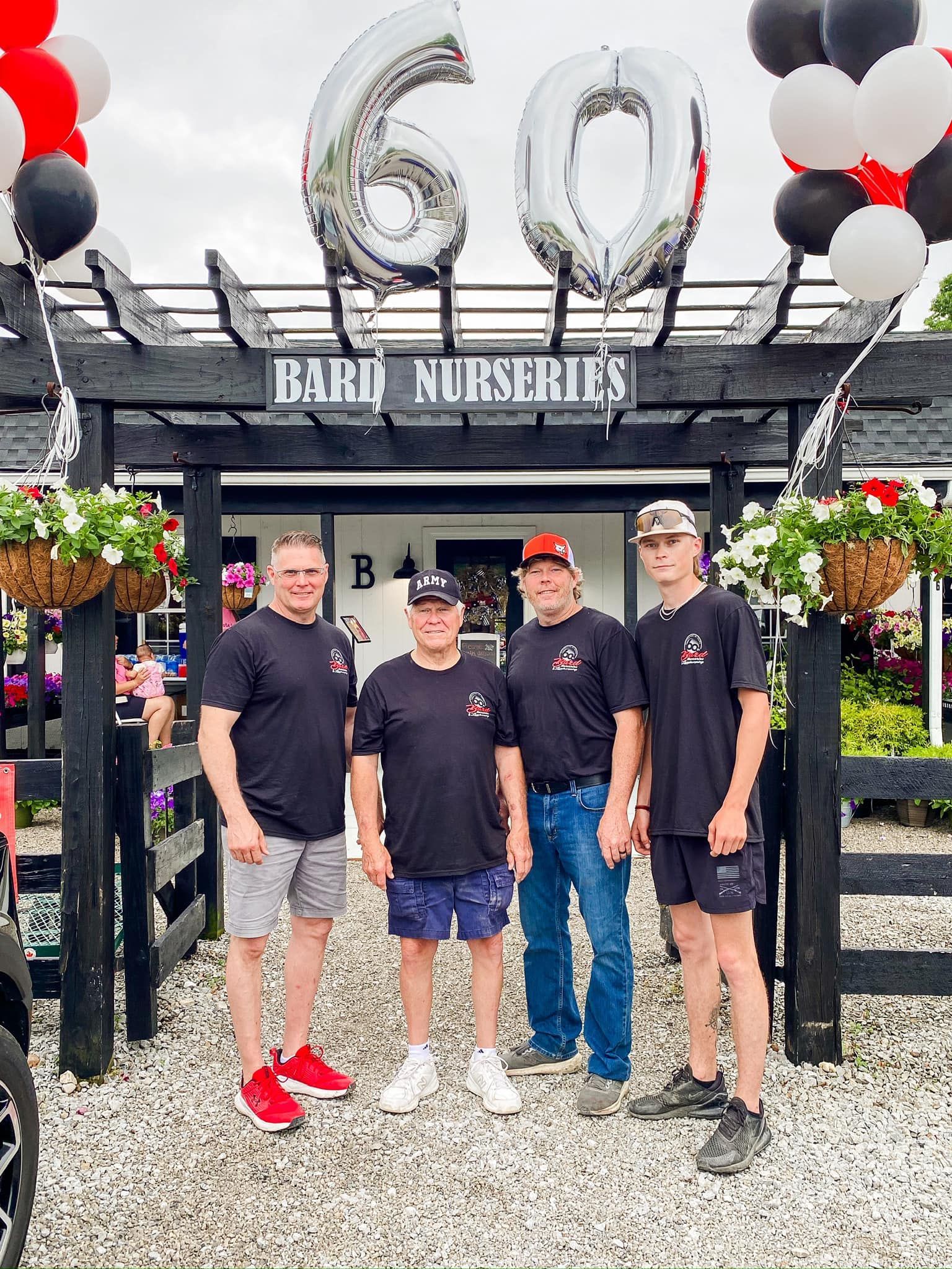 Four men pose in front of a nursery entrance decorated with balloons, flowers, and a 