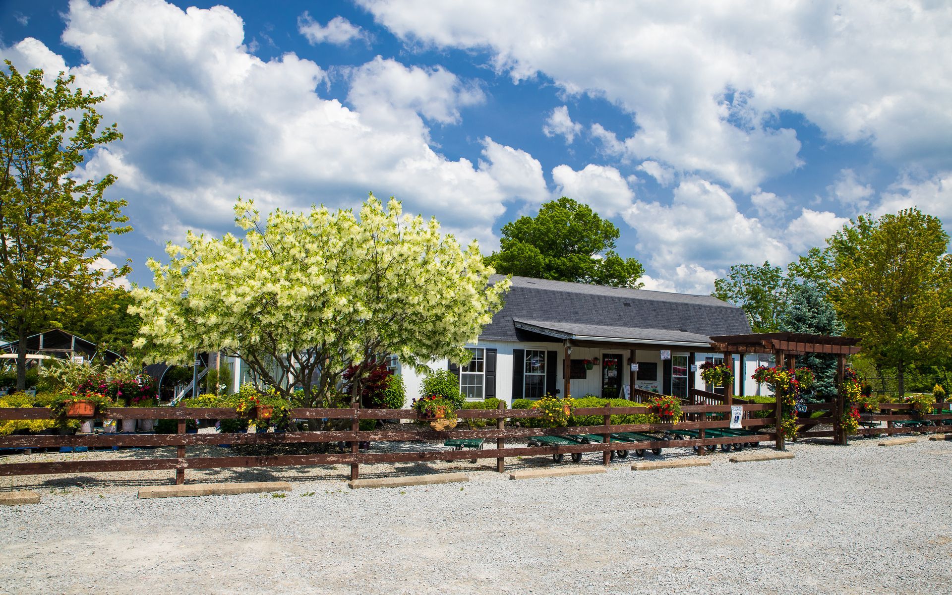 White building with black roof, outdoor seating, surrounded by trees, blue sky with clouds.