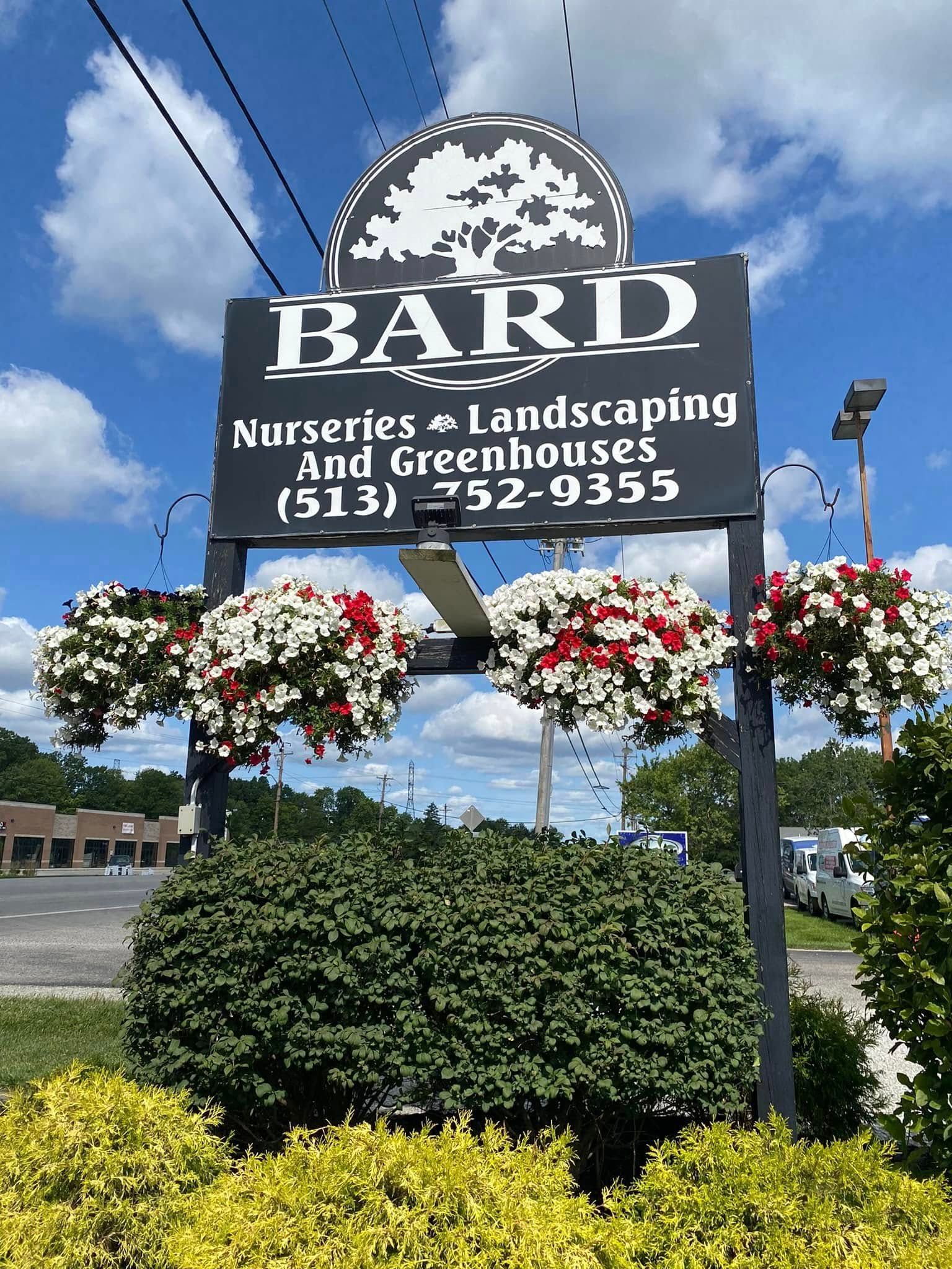 Sign for Bard Nurseries with hanging flower baskets and phone number.
