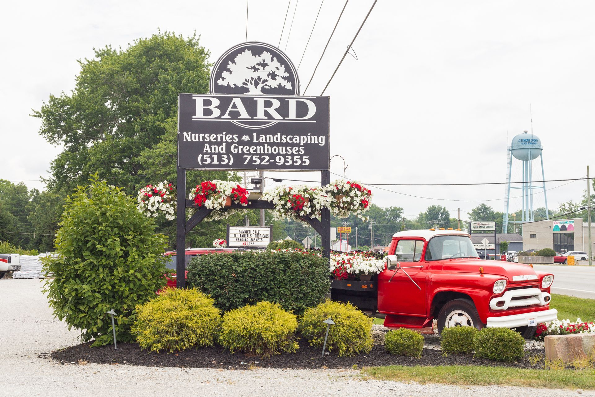 Bard Nurseries sign with red truck, flowers, landscaping, and water tower in the background.