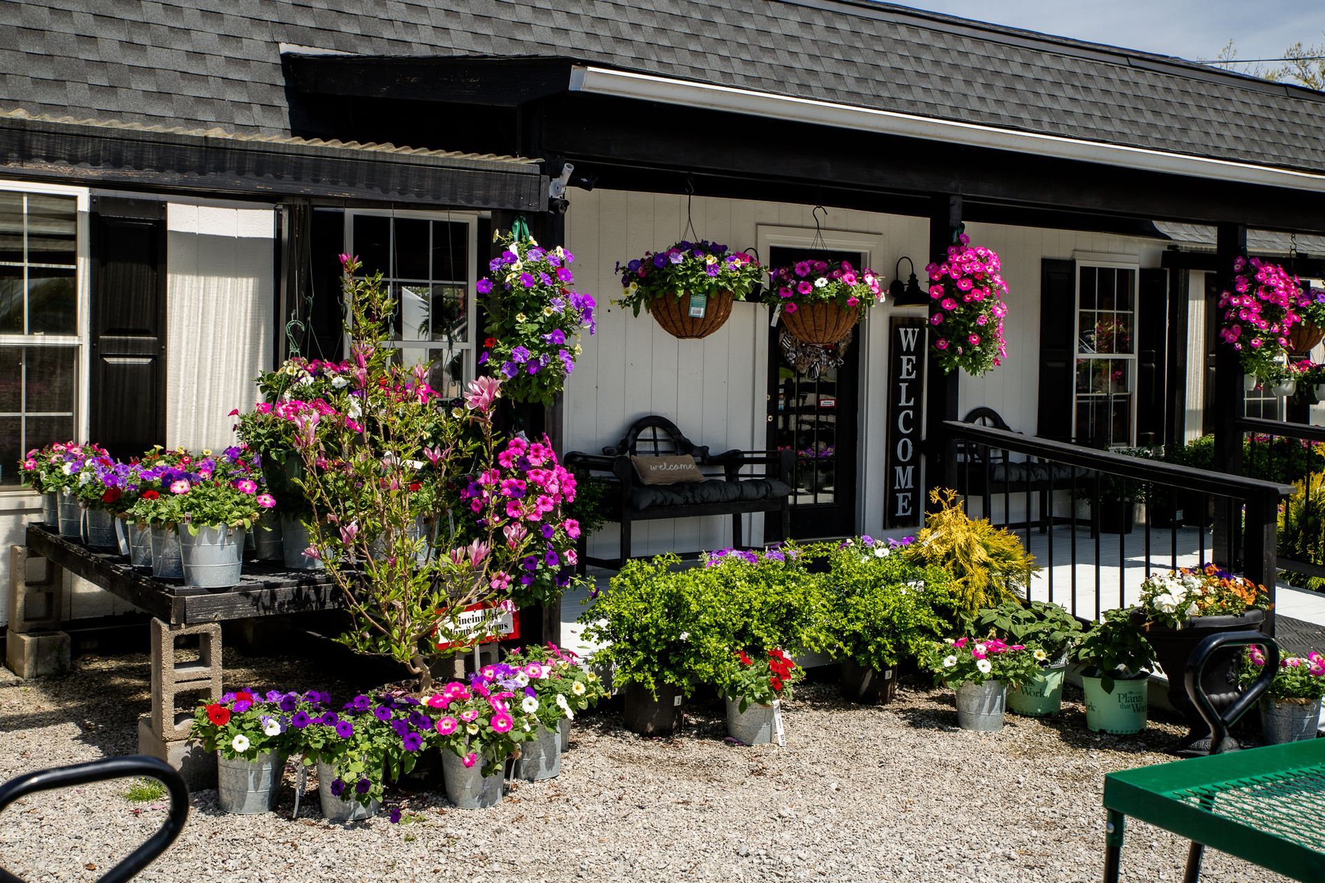 Exterior of a white building with black trim, overflowing with colorful potted flowers.