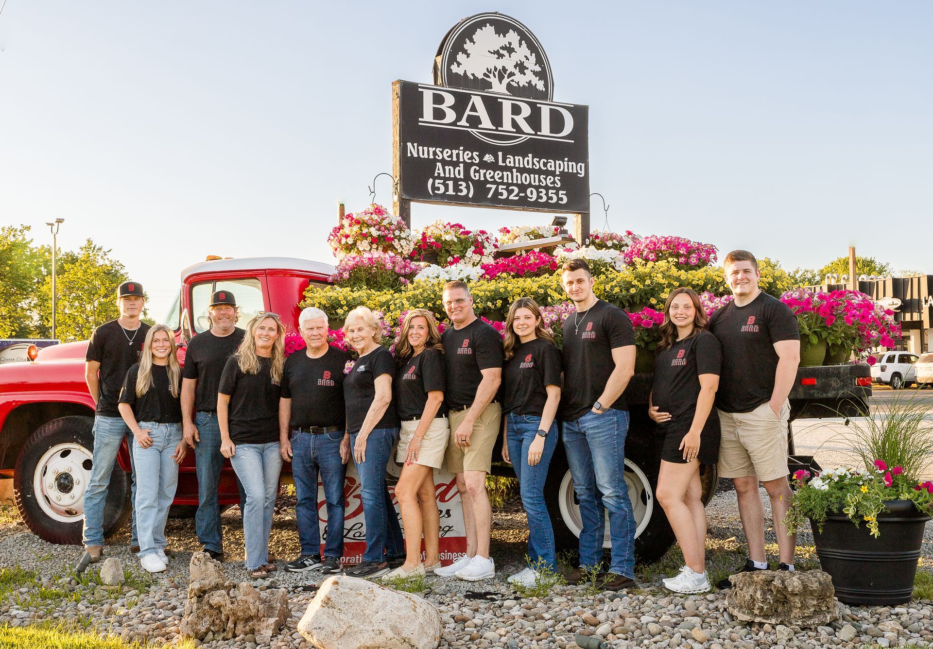 A group poses in front of a red truck with flowers; the sign above says 