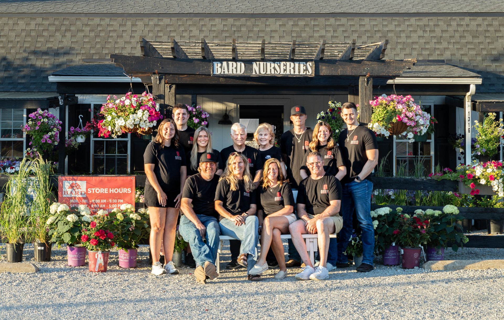Employees of Bard Nurseries pose for a group photo in front of the store with hanging flowers.