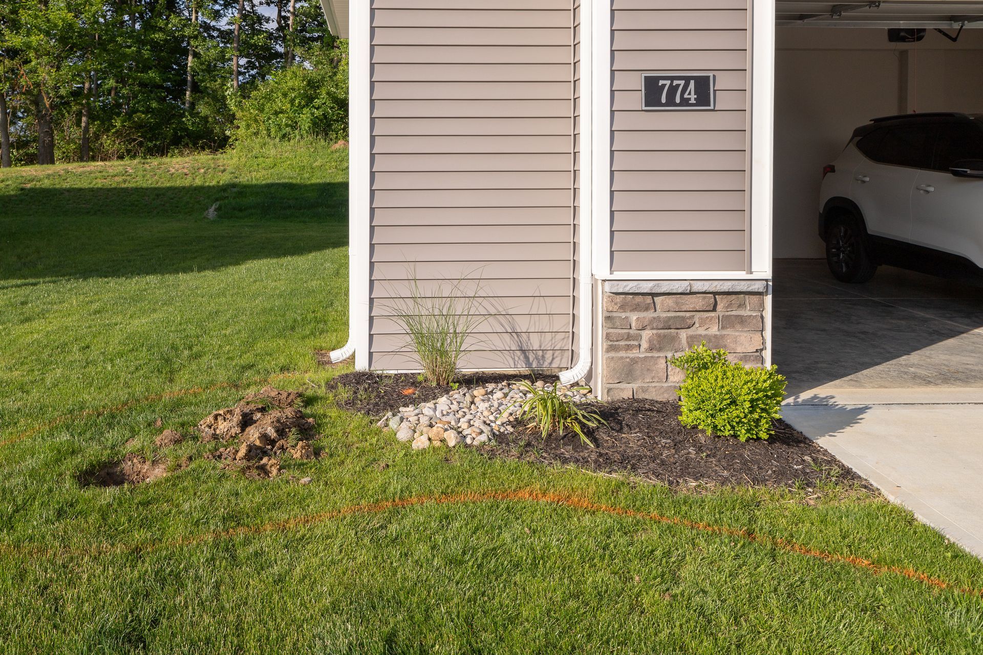 House exterior with landscaping, mulch, rocks, and a grassy lawn; a car parked in the garage.