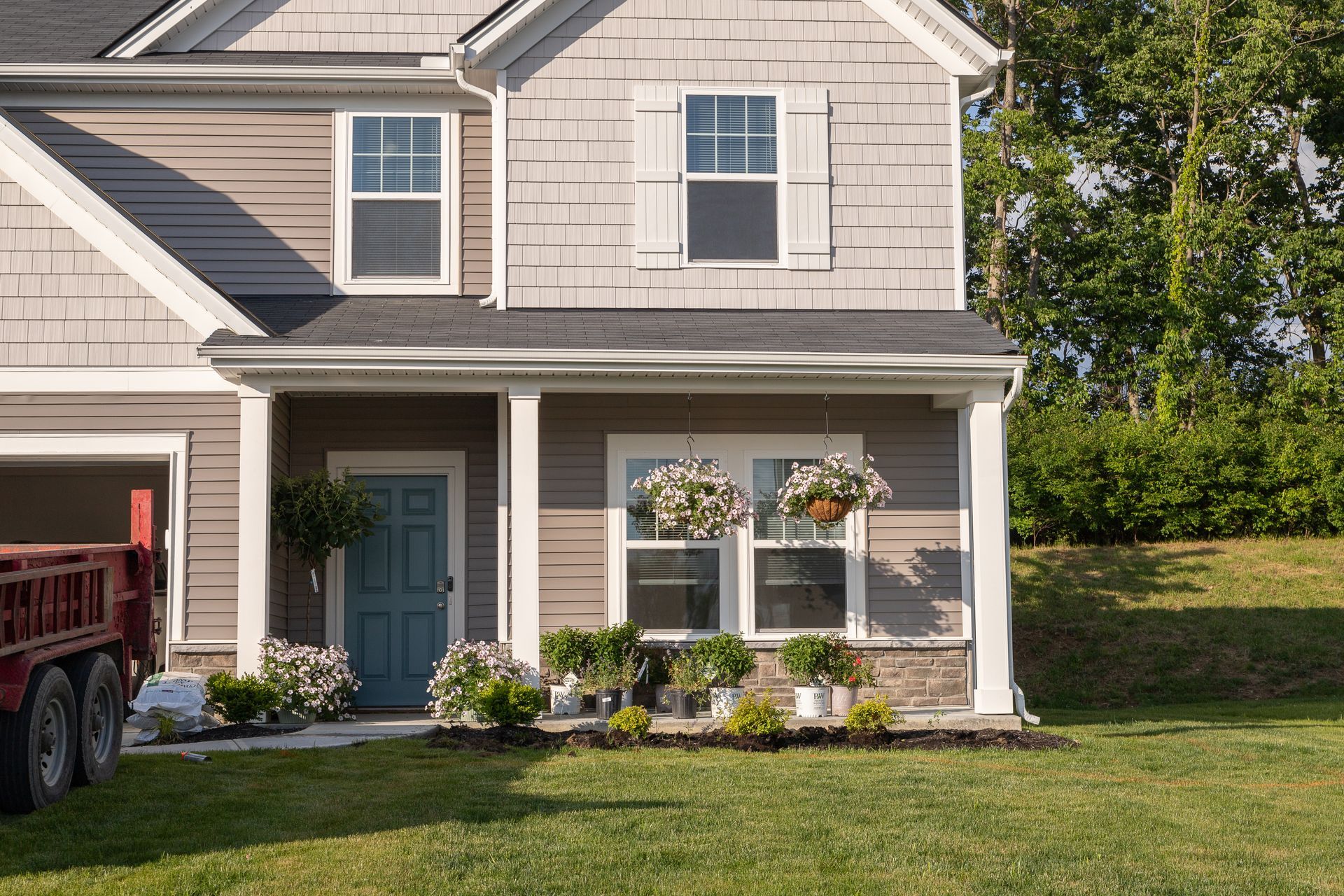 Two-story house with gray and tan siding. Blue door, hanging flower baskets, and flower beds.