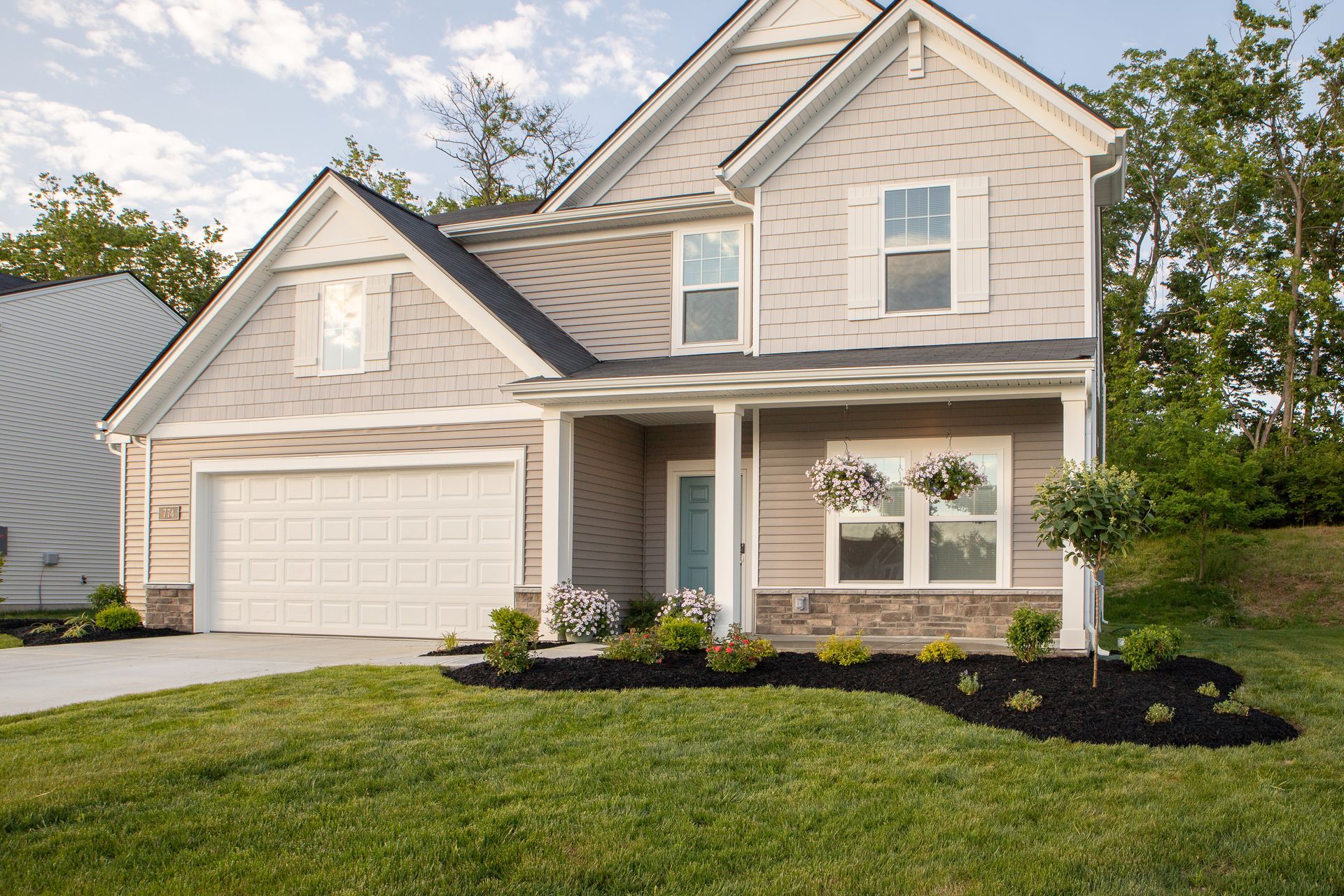 Two-story house with gray siding, white garage door, small porch, and manicured lawn.