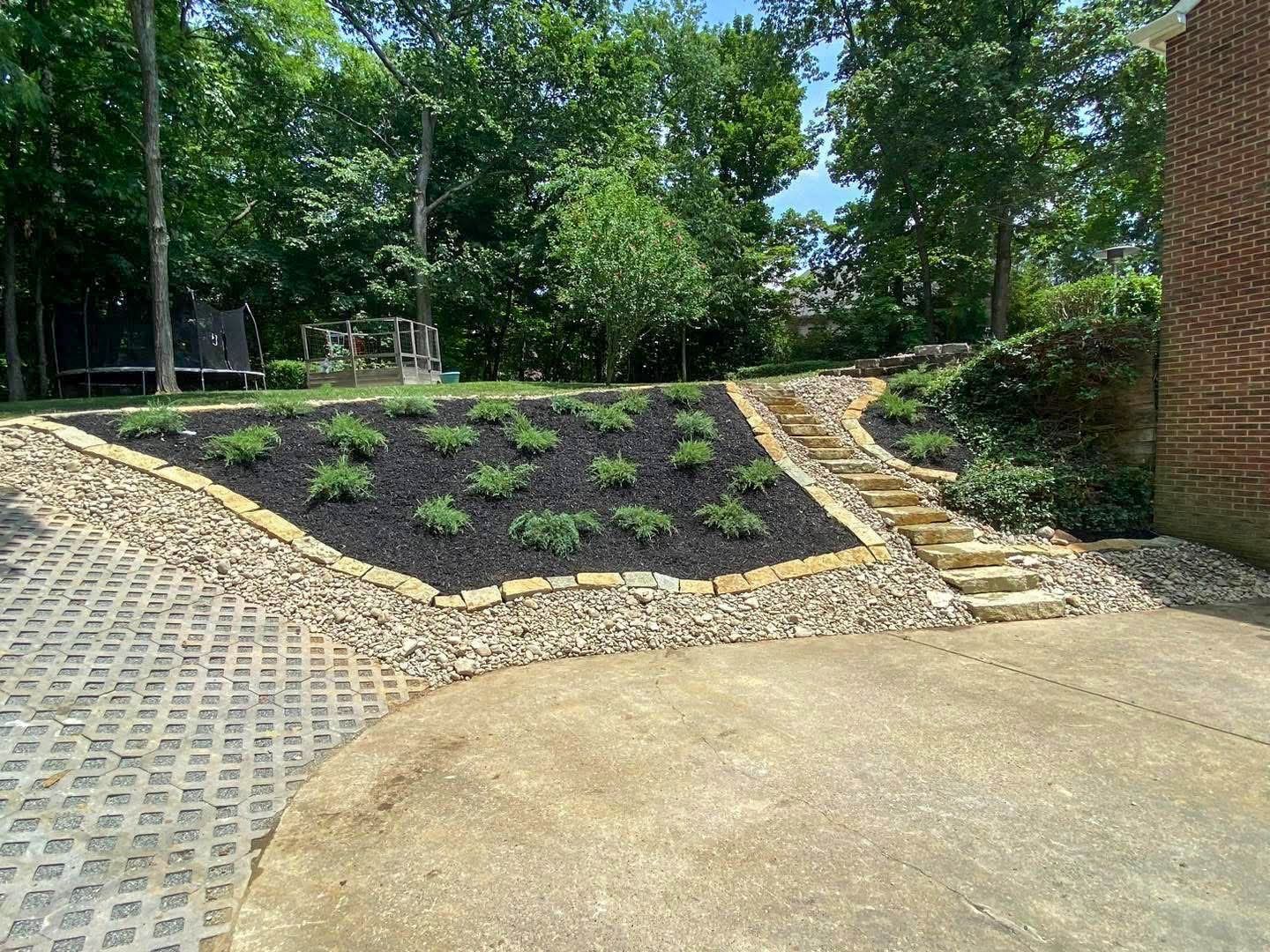 Landscaped backyard with mulch bed and stone steps leading up the slope.