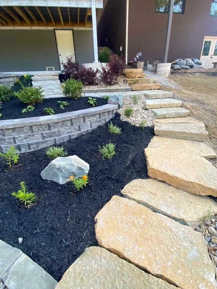 Landscaped backyard with stone steps, retaining wall, dark mulch, and various plants.