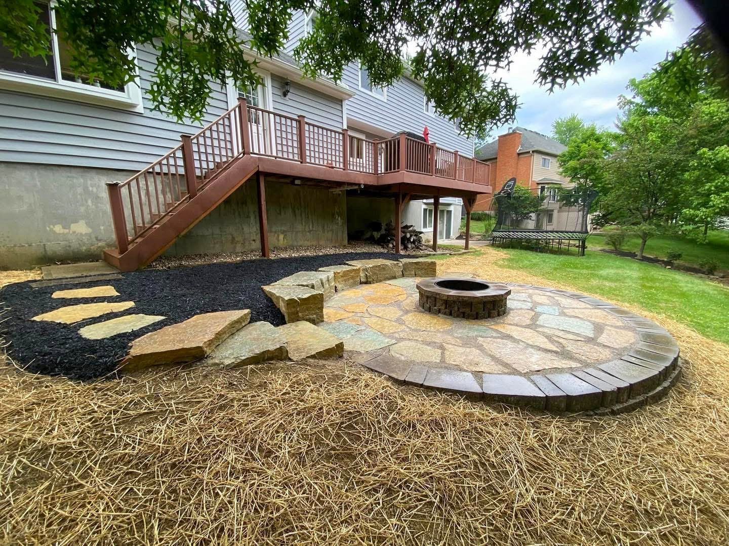 Backyard patio with fire pit, steps, and deck under a two-story house.