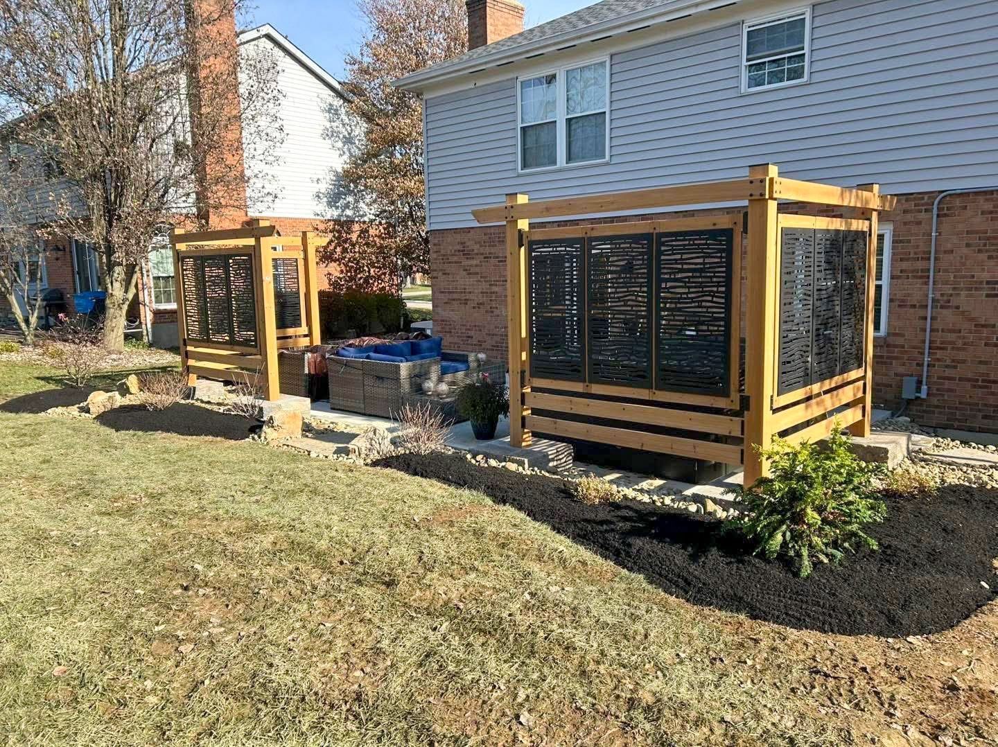 Two wooden framed screens with black panel inserts in a backyard, near a brick house.