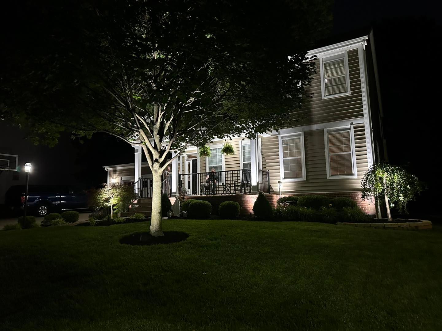 Two-story house illuminated at night with a tree and landscaping in the front yard.