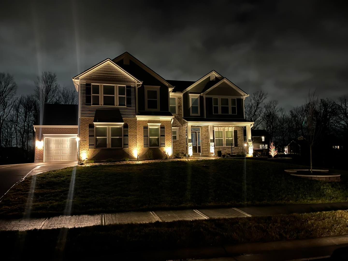 House illuminated at night with landscape lighting and a cloudy sky.