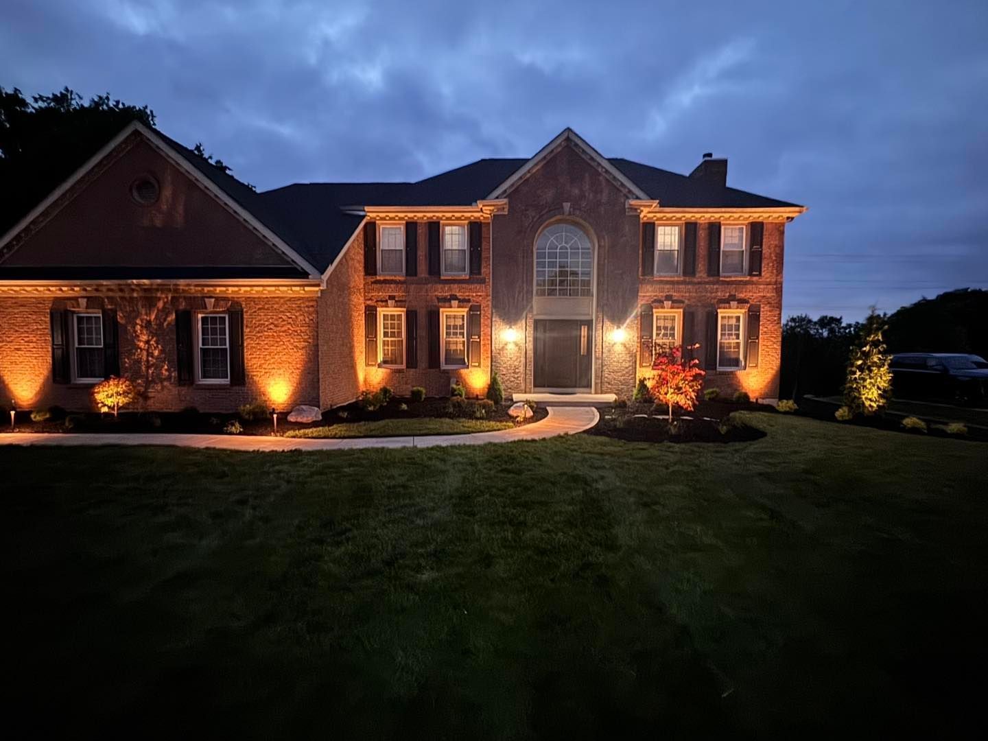 Well-lit garden path with trees, bushes, and decorative lights.