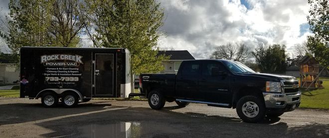 Black lifted pickup truck parked beside a black trailer in a sunny outdoor lot.