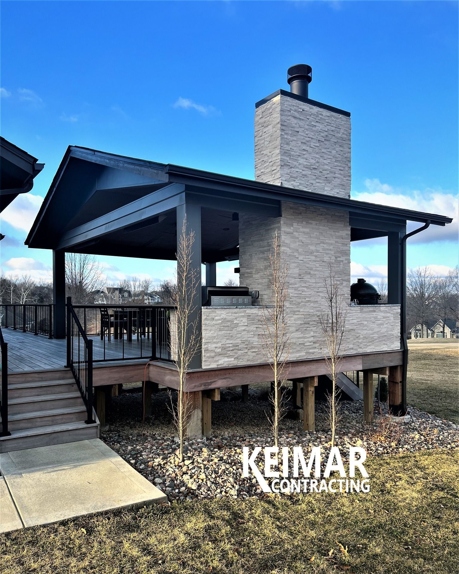 Outdoor kitchen and dining area with a brick chimney and a deck on a sunny day.