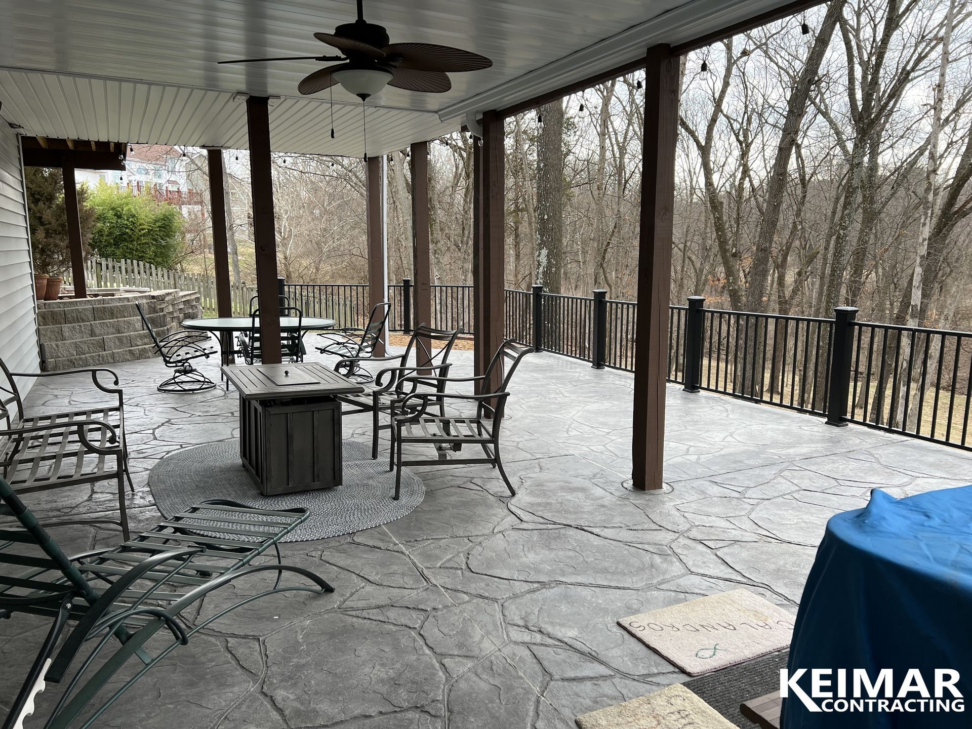 Covered patio with stamped concrete floor, outdoor furniture, and a forested view.