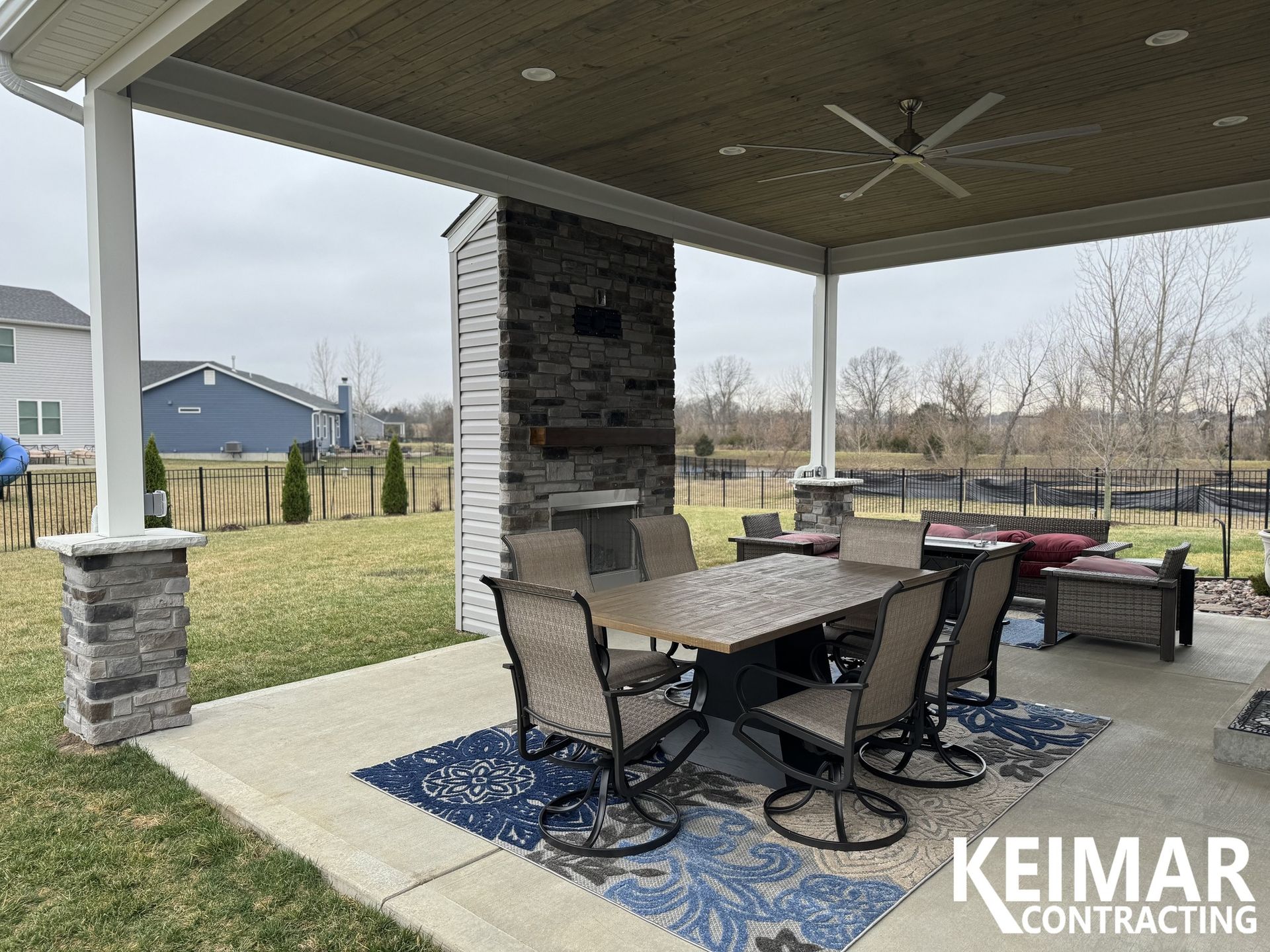 Covered patio with dining table, outdoor fireplace, and view of a backyard.