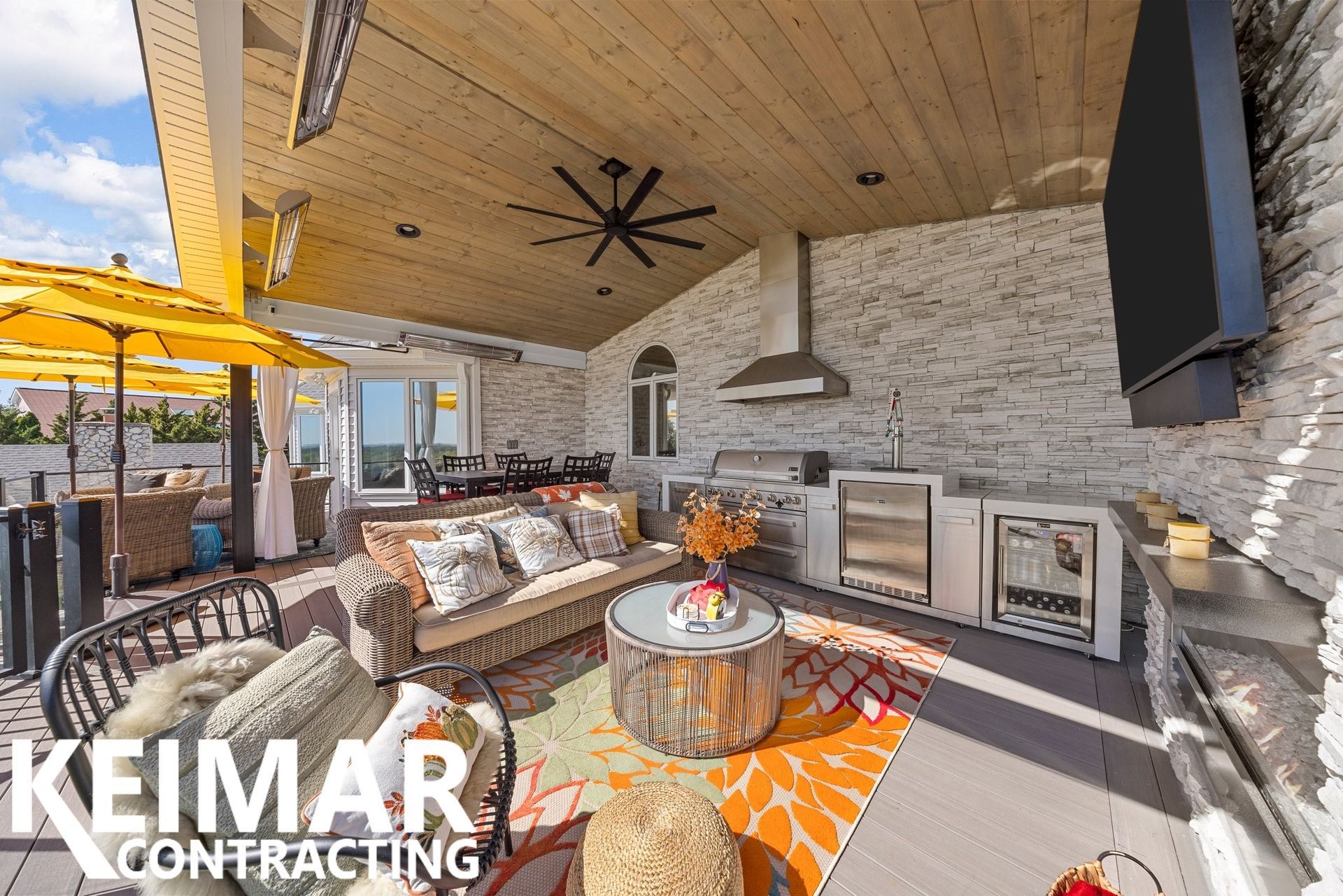 Outdoor kitchen and lounge area with white brick, wooden ceiling, and colorful rugs.