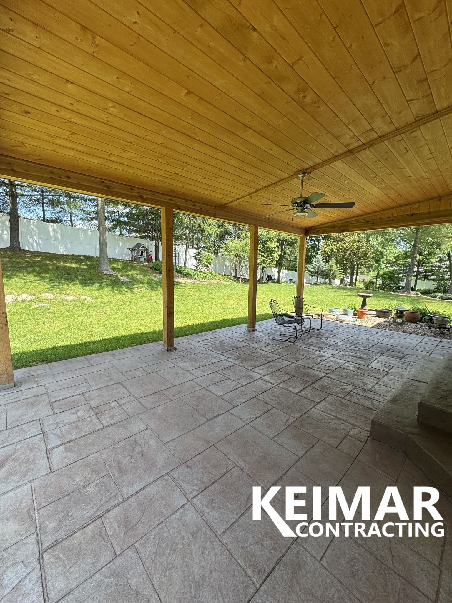 Covered patio with stamped concrete floor and wooden ceiling, overlooking a grassy yard.