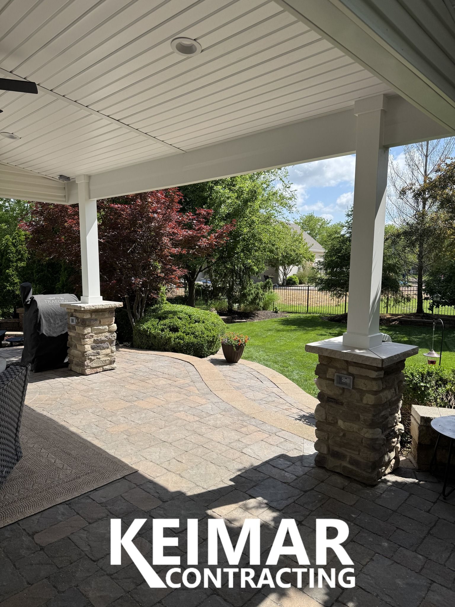 Covered patio with stone pillars, pavers, and a view of a backyard.