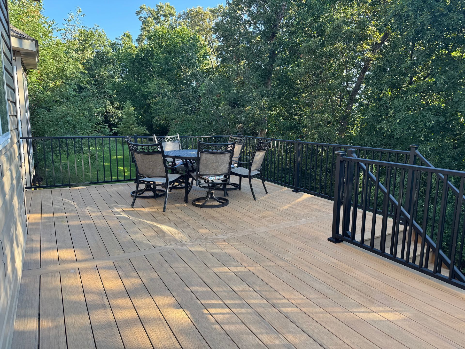 Composite deck with black railing and outdoor dining set, surrounded by trees.