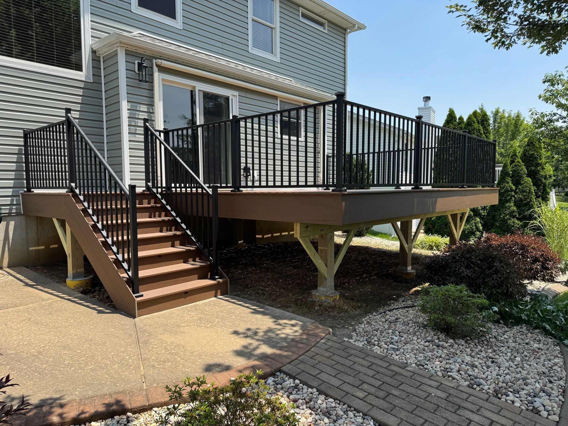 Deck with black railing, stairs, and light brown composite decking. House with light blue siding in the background.