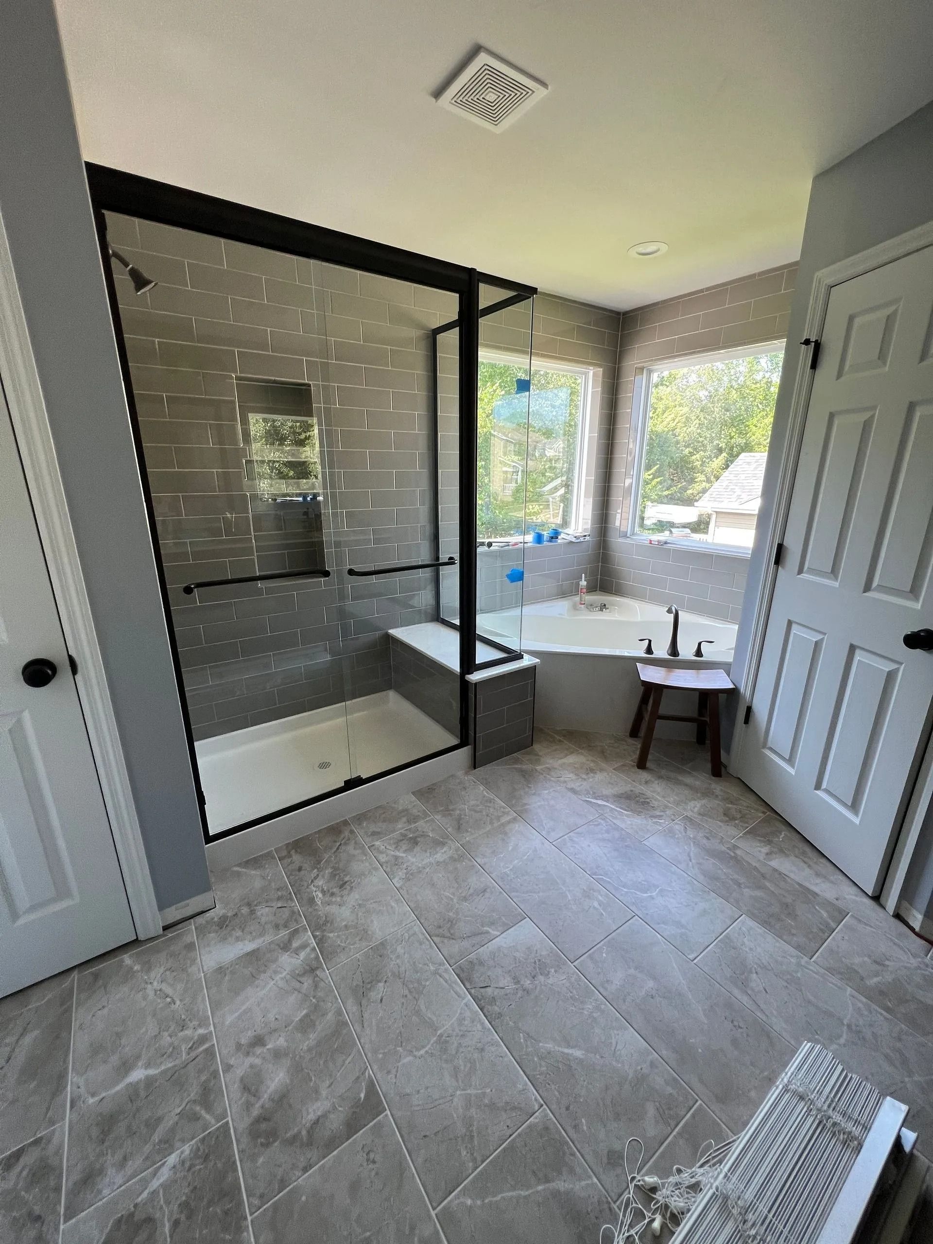Modern bathroom with a glass shower, soaking tub, and gray tile flooring.