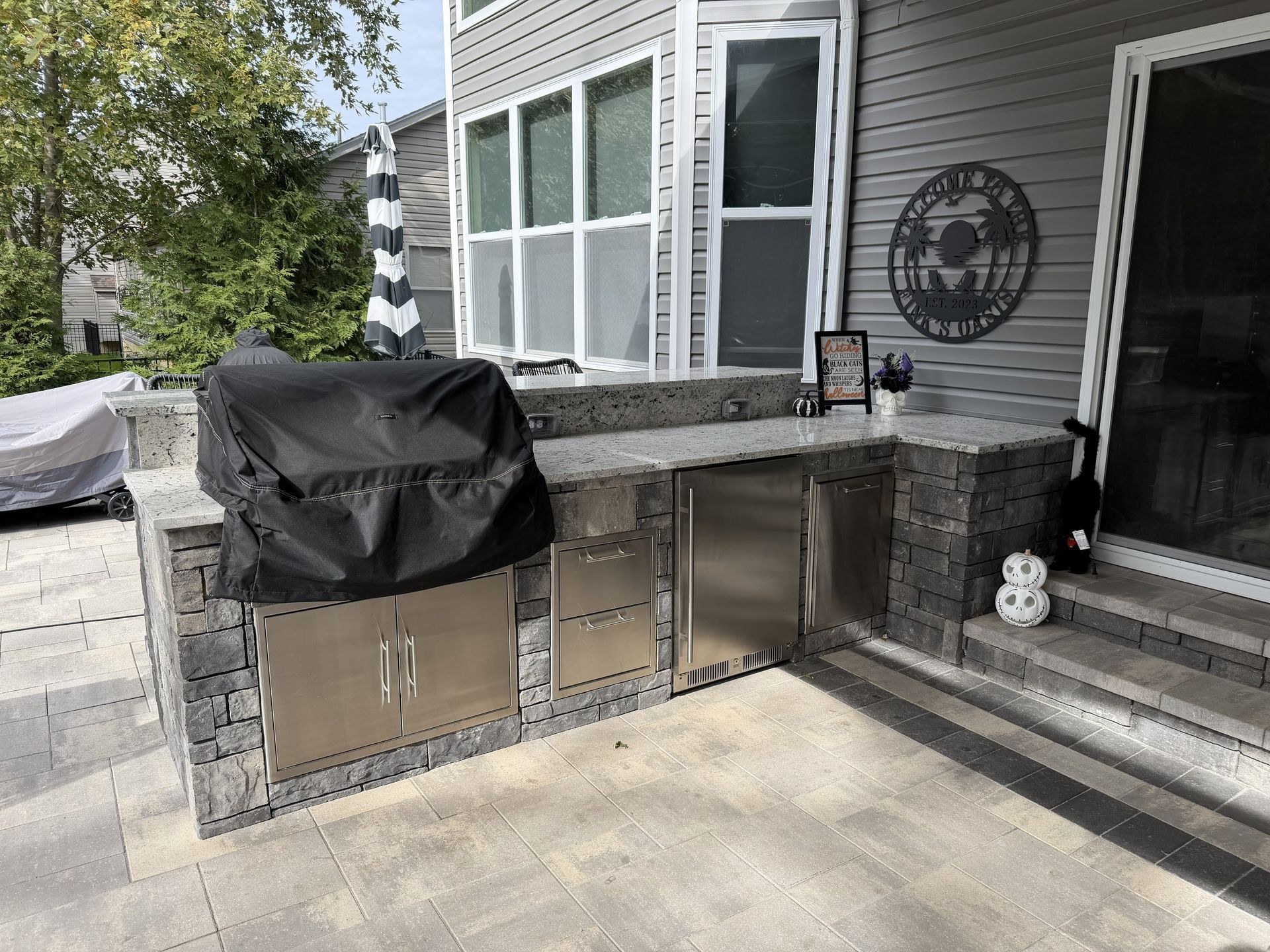Outdoor kitchen with grill, stainless steel appliances, and stone countertop on a patio.