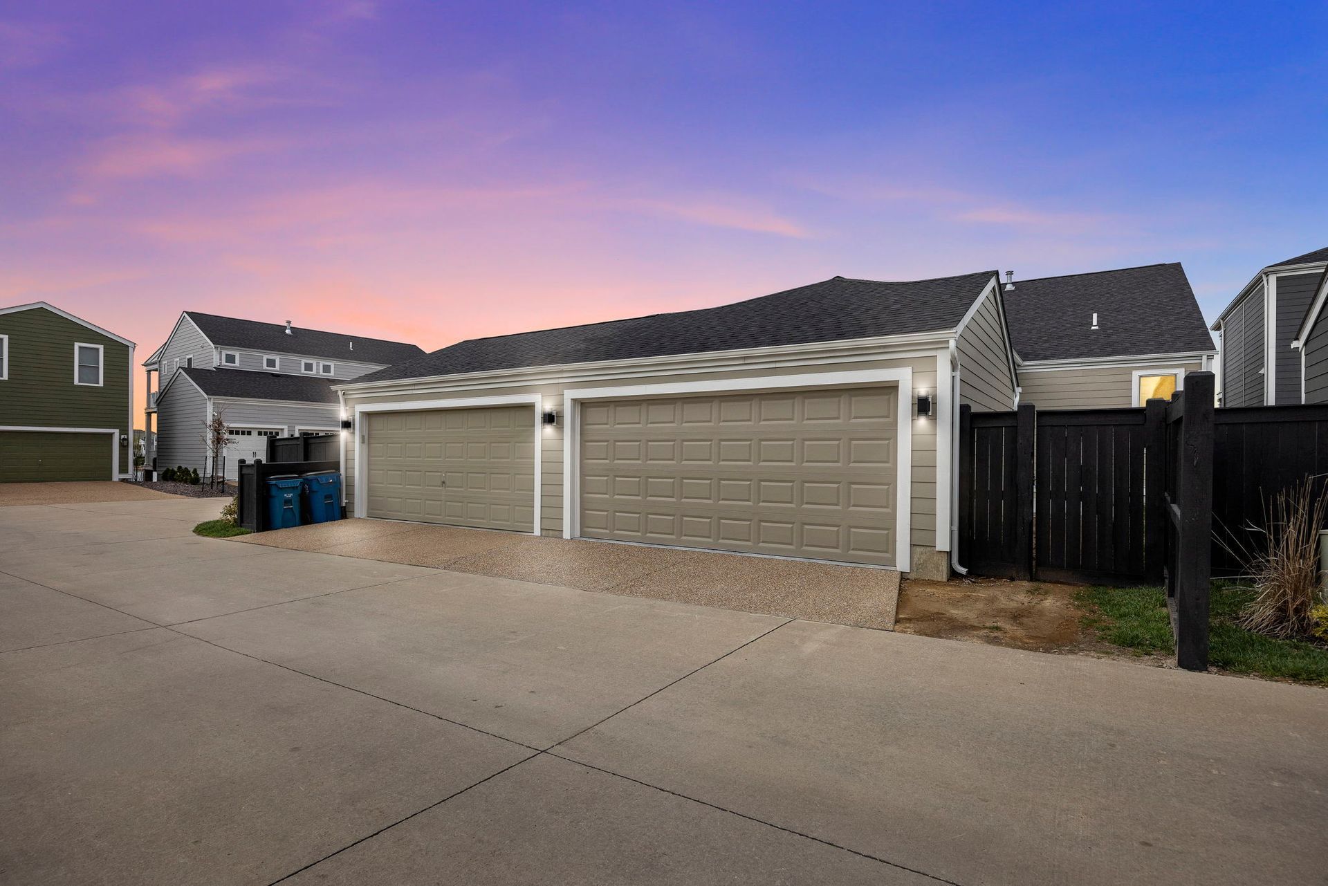 Two-car garage with gray doors, light siding, and black roof, at dusk.