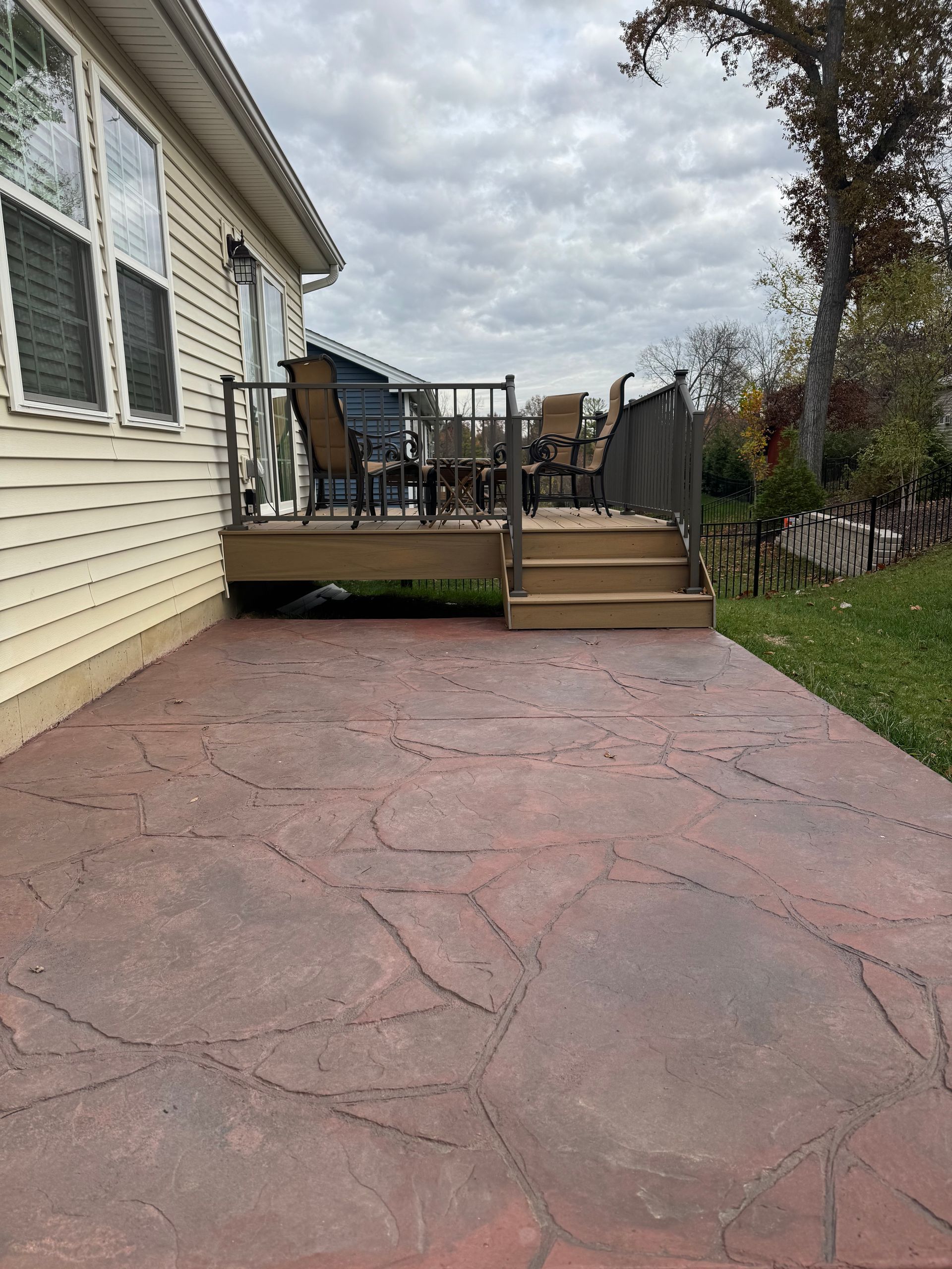 Red stamped concrete patio leading to wooden deck with steps. Cloudy day.