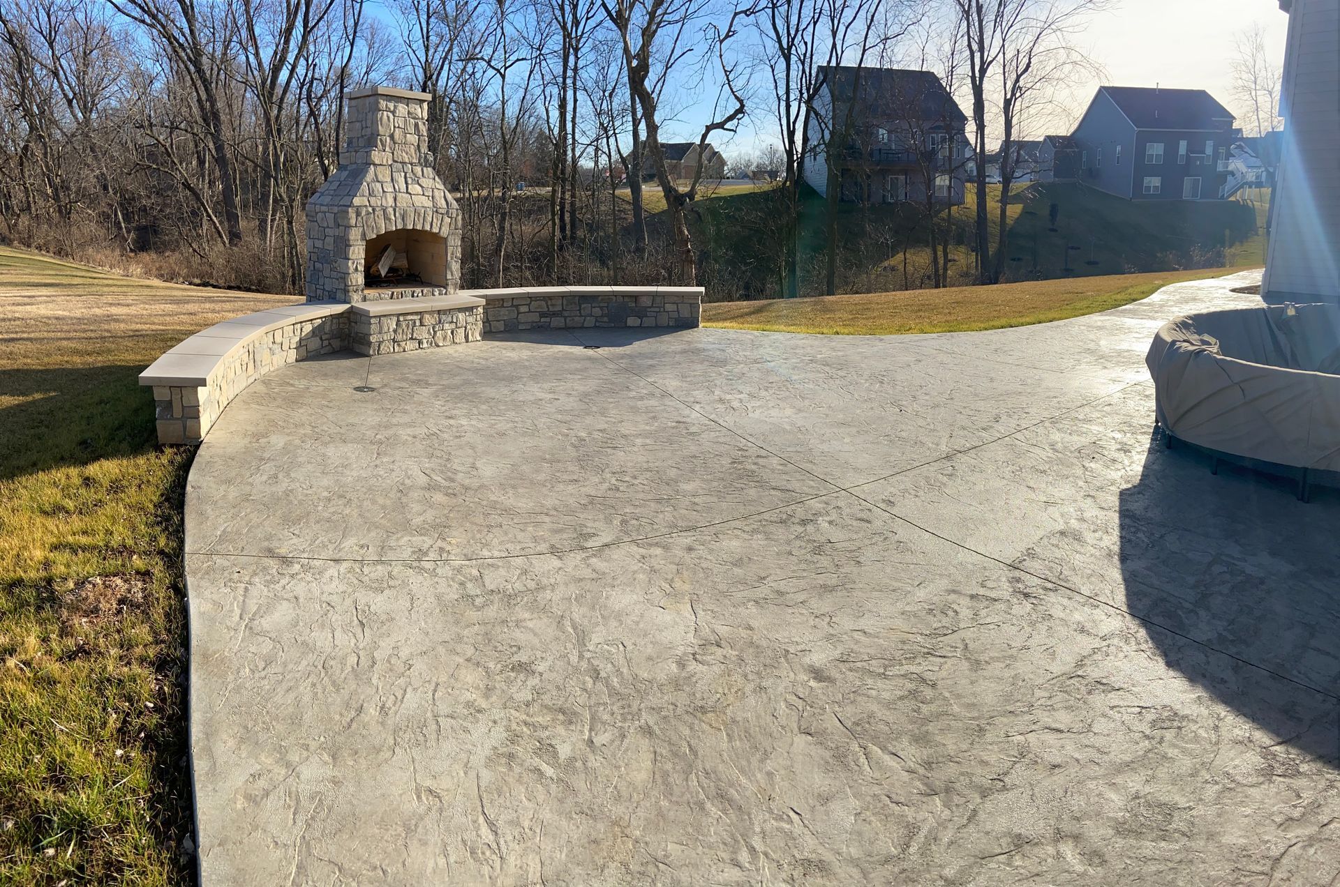 Outdoor patio with fireplace, built-in seating, and a view of houses and trees.