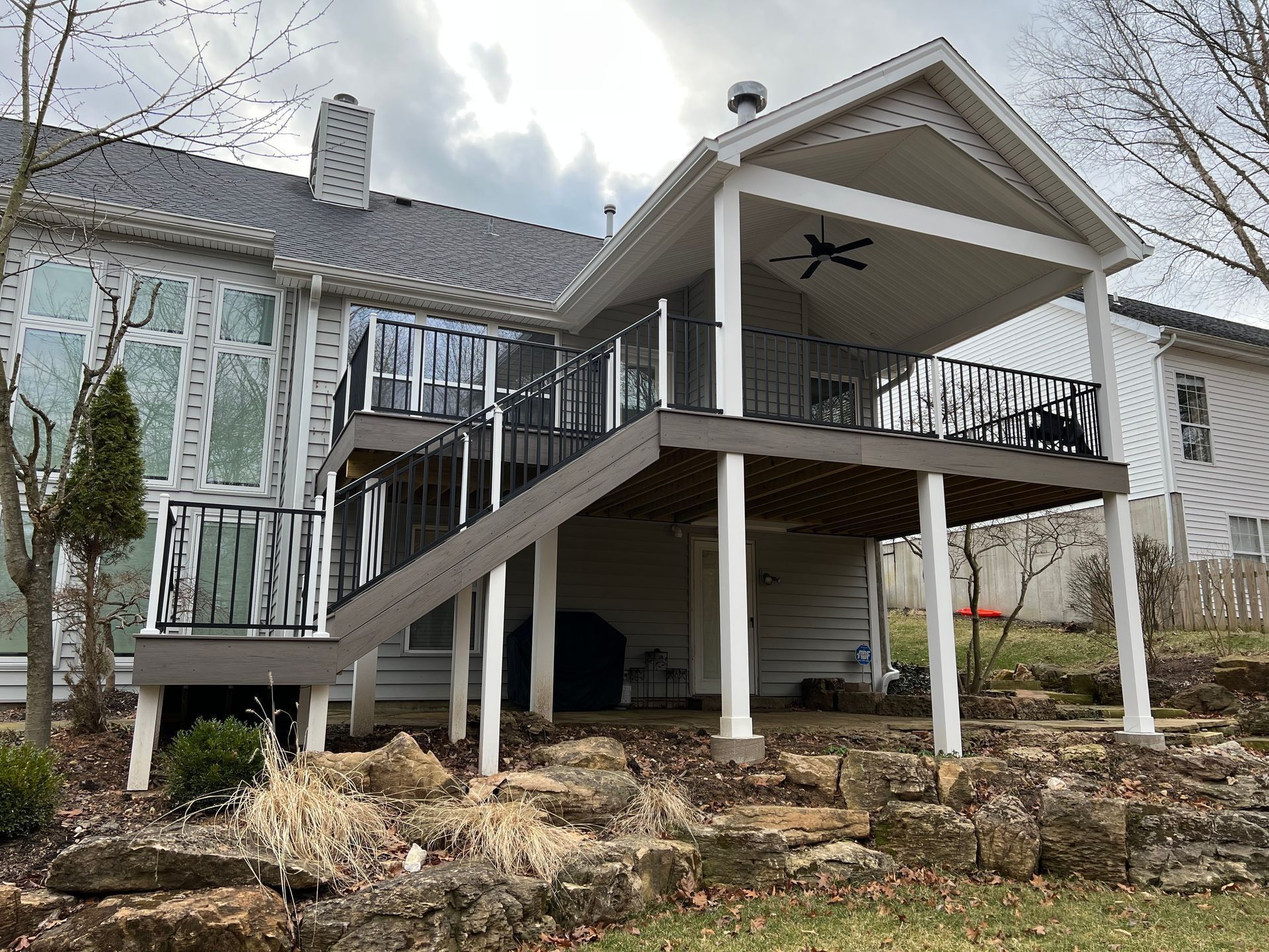 Multi-level deck with black railing and covered upper deck attached to a house with a stone retaining wall.