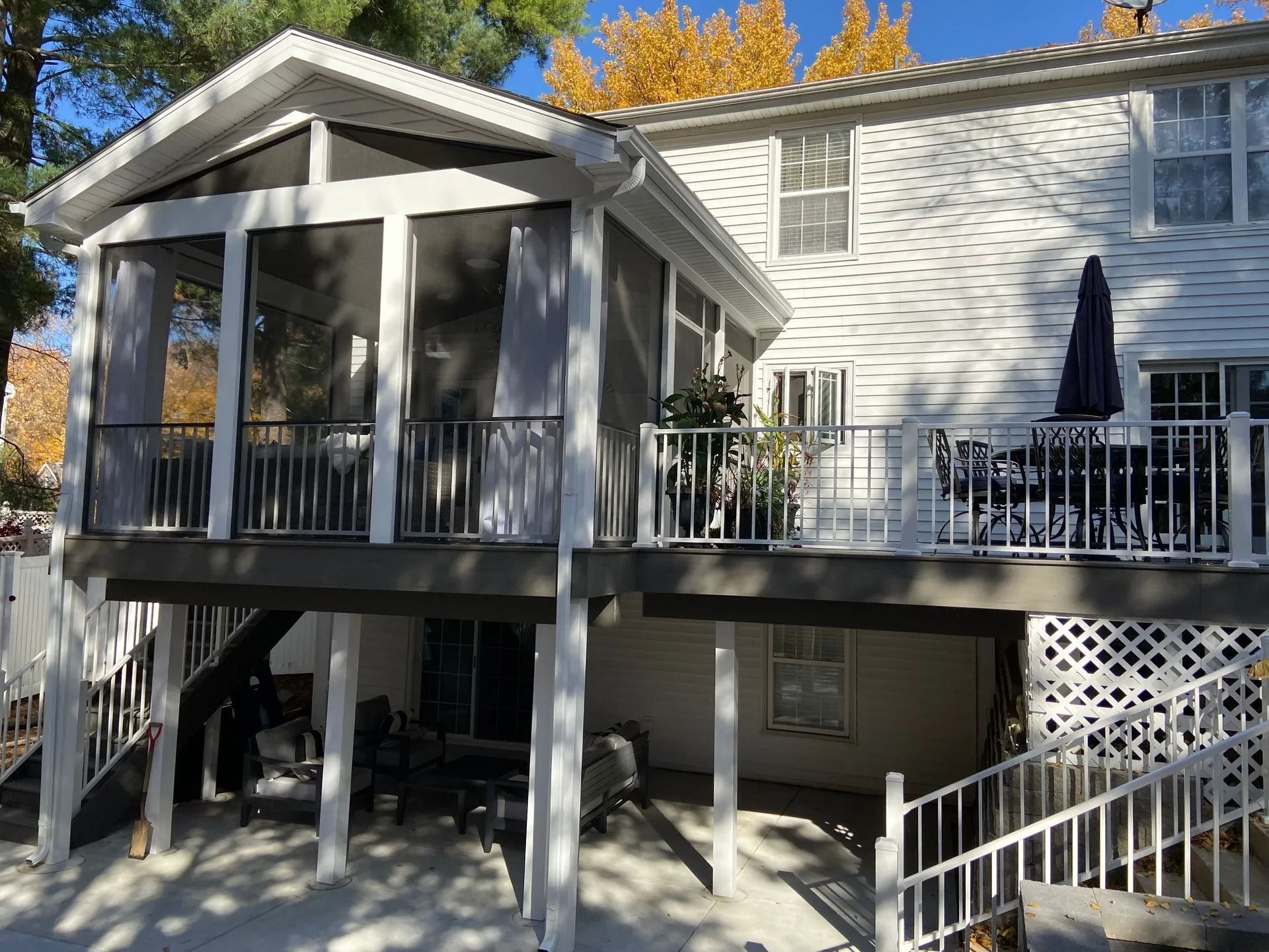 Two-story house with a screened porch and deck; white siding, dark gray trim, and blue umbrella.