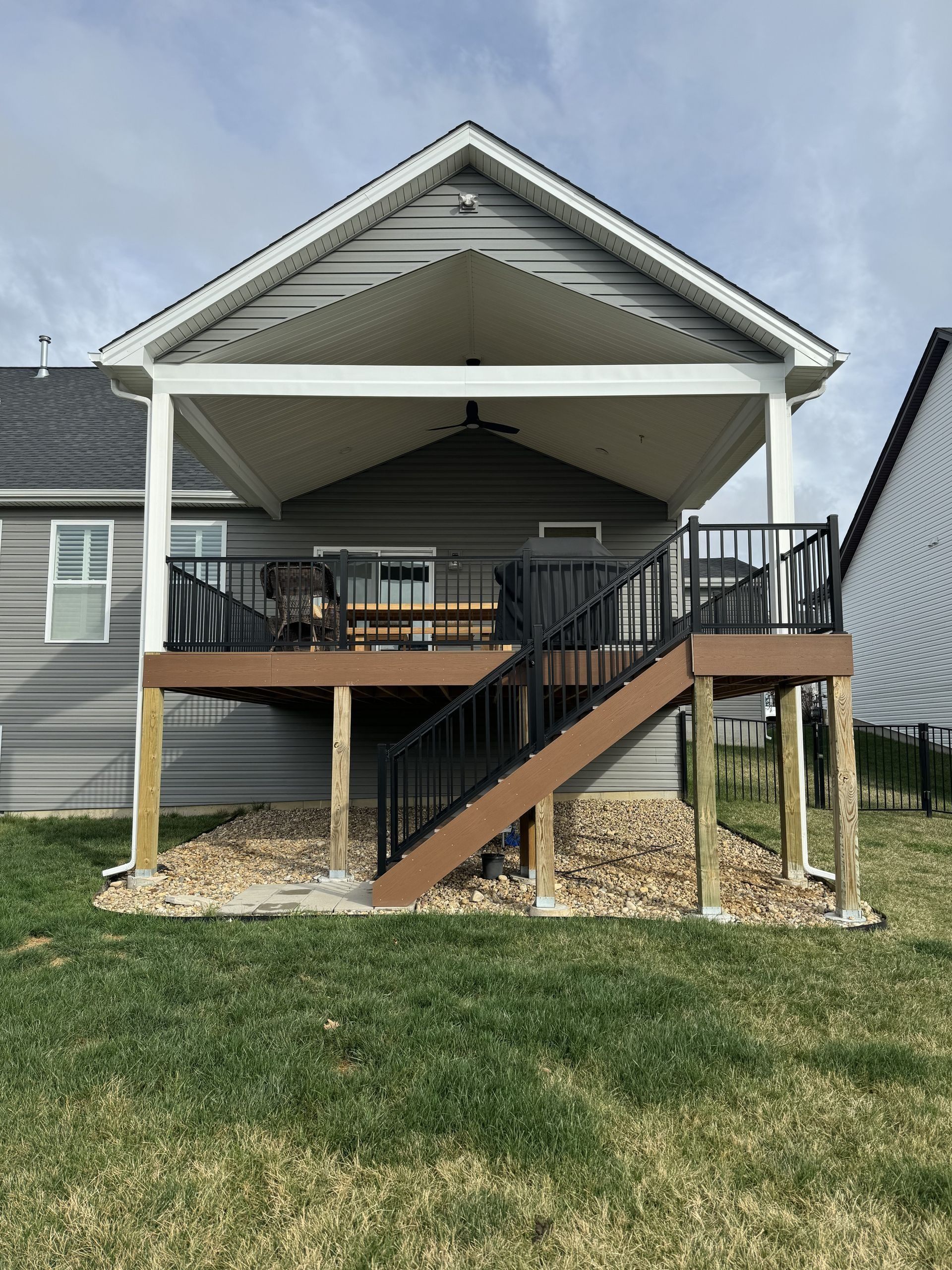 House with a covered deck, stairs, black railing, and a brown deck, with a grassy yard.