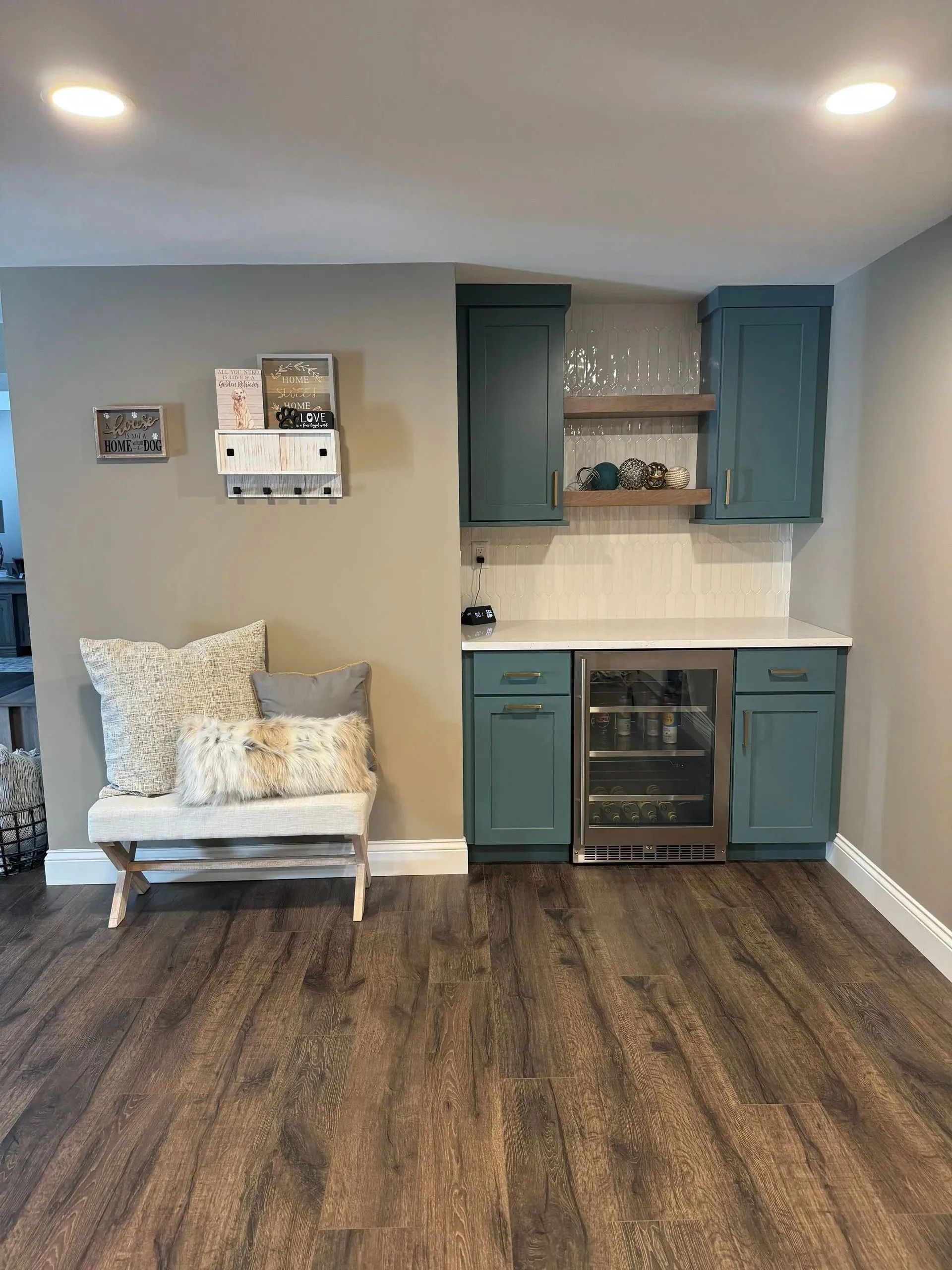 Living space with wood-look floor, bench with pillows, and blue cabinets with a beverage fridge.