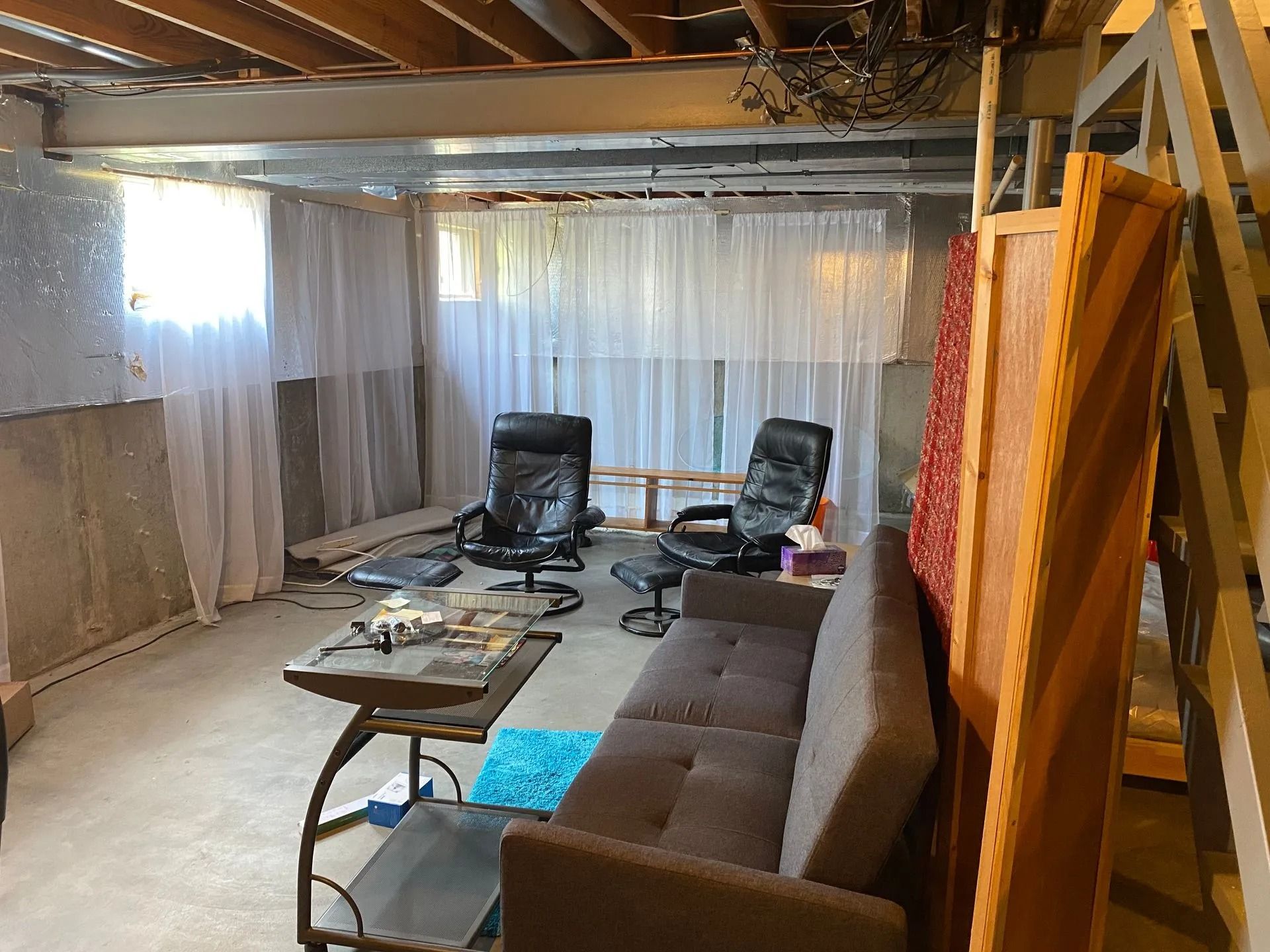 Basement living space with a couch, two chairs, a coffee table, and a partially covered window.