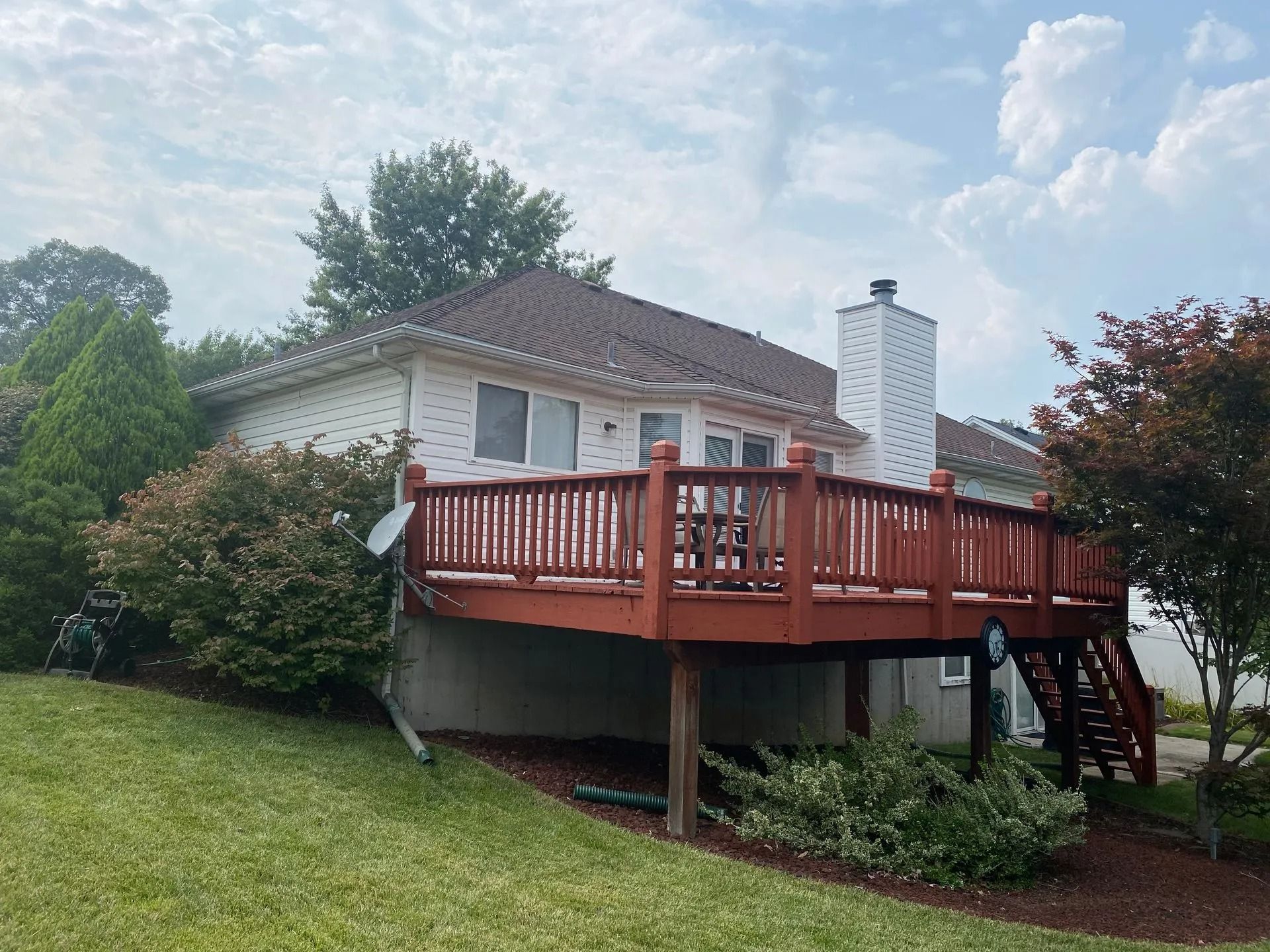 House with red deck, white brick, brown roof, chimney, and surrounding greenery.
