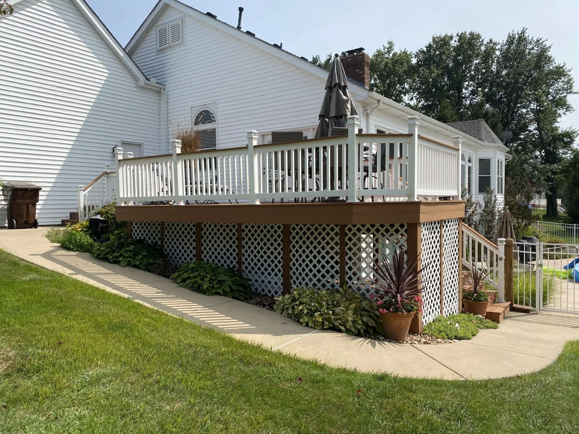 White house with a large wooden deck and lattice skirting, with a curved sidewalk in the yard.