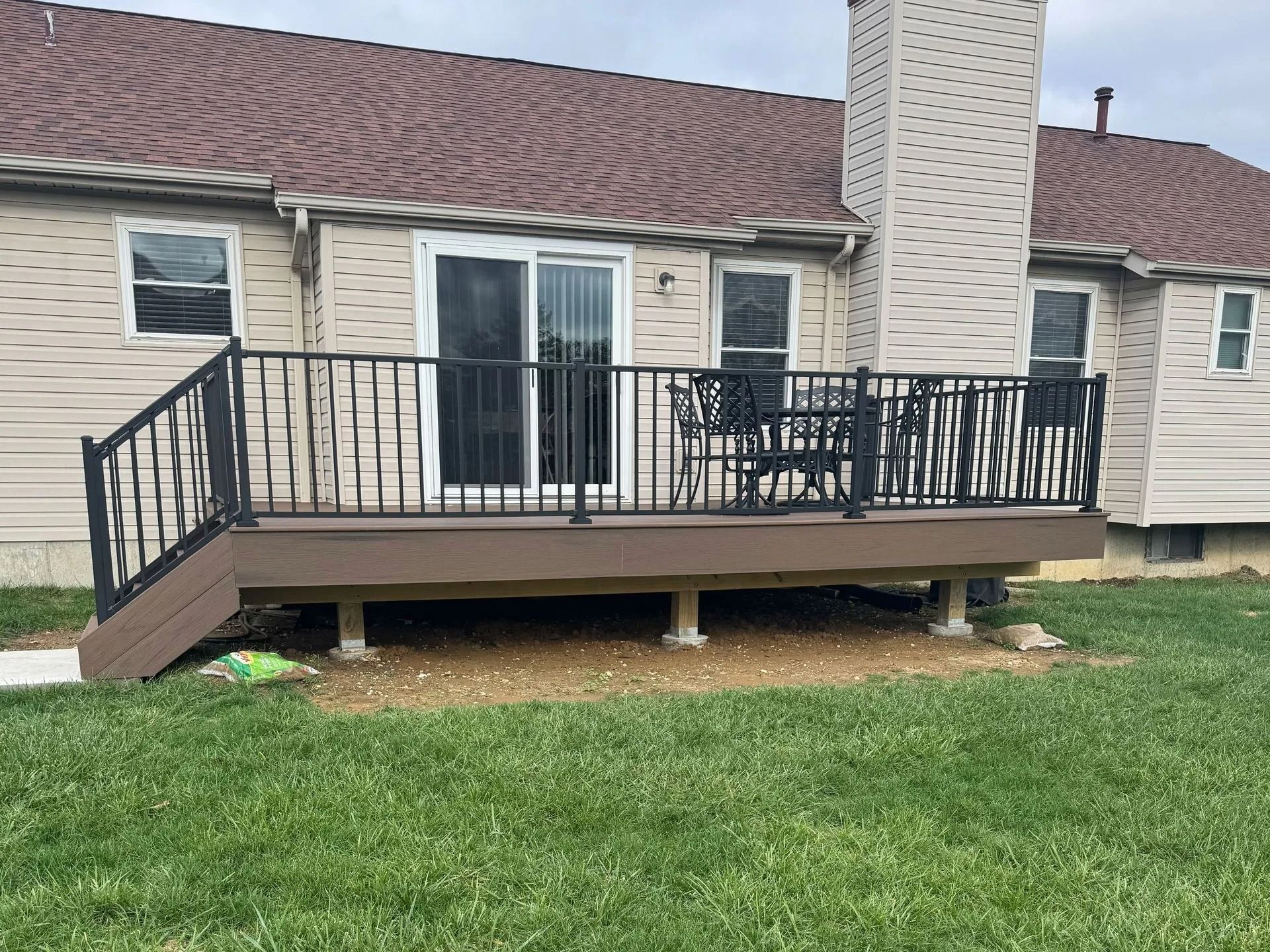 Composite deck with black railing and sliding door, beige house, and green lawn.