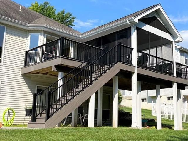 Multi-level deck with black railing and screened porch. Exterior of a house with green lawn.