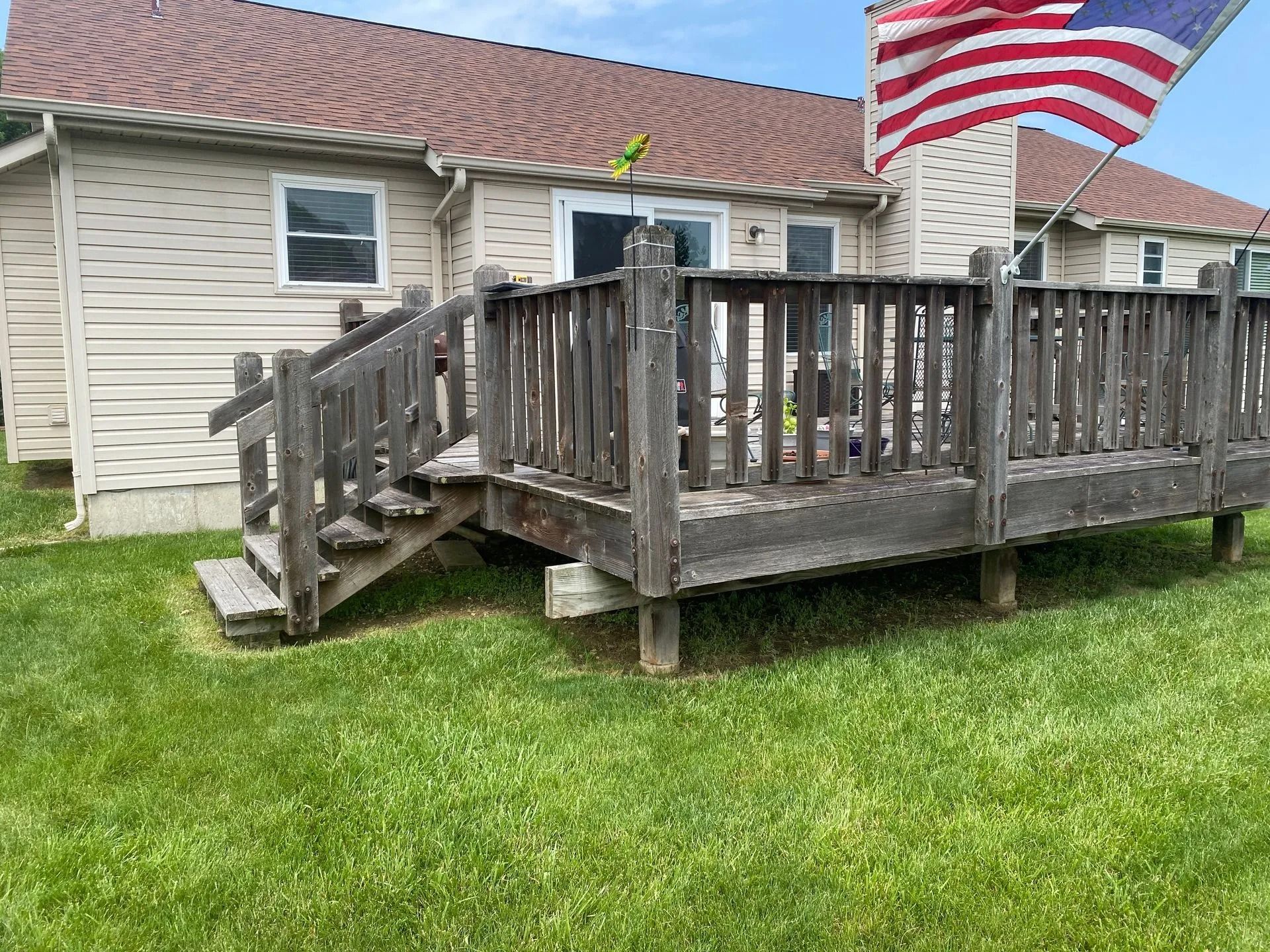 Wooden deck attached to a house with an American flag blowing in the wind.