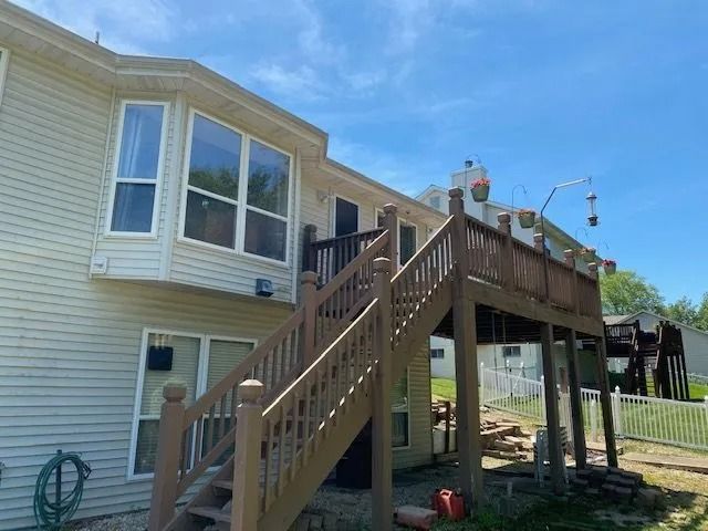 Back of a two-story beige house with a wooden deck and stairs, with blue sky above.