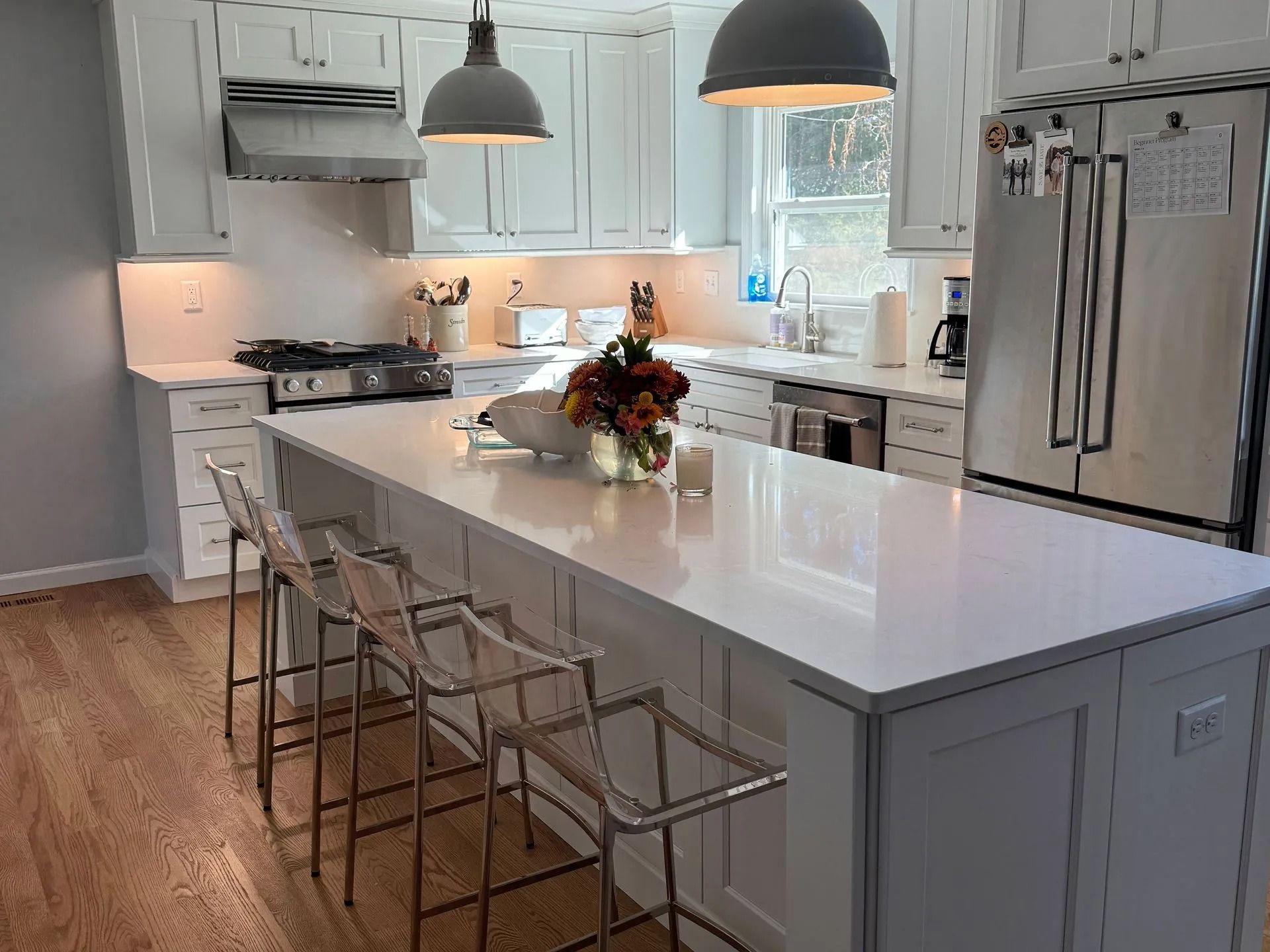 White kitchen with an island, stainless steel appliances, and clear bar stools.