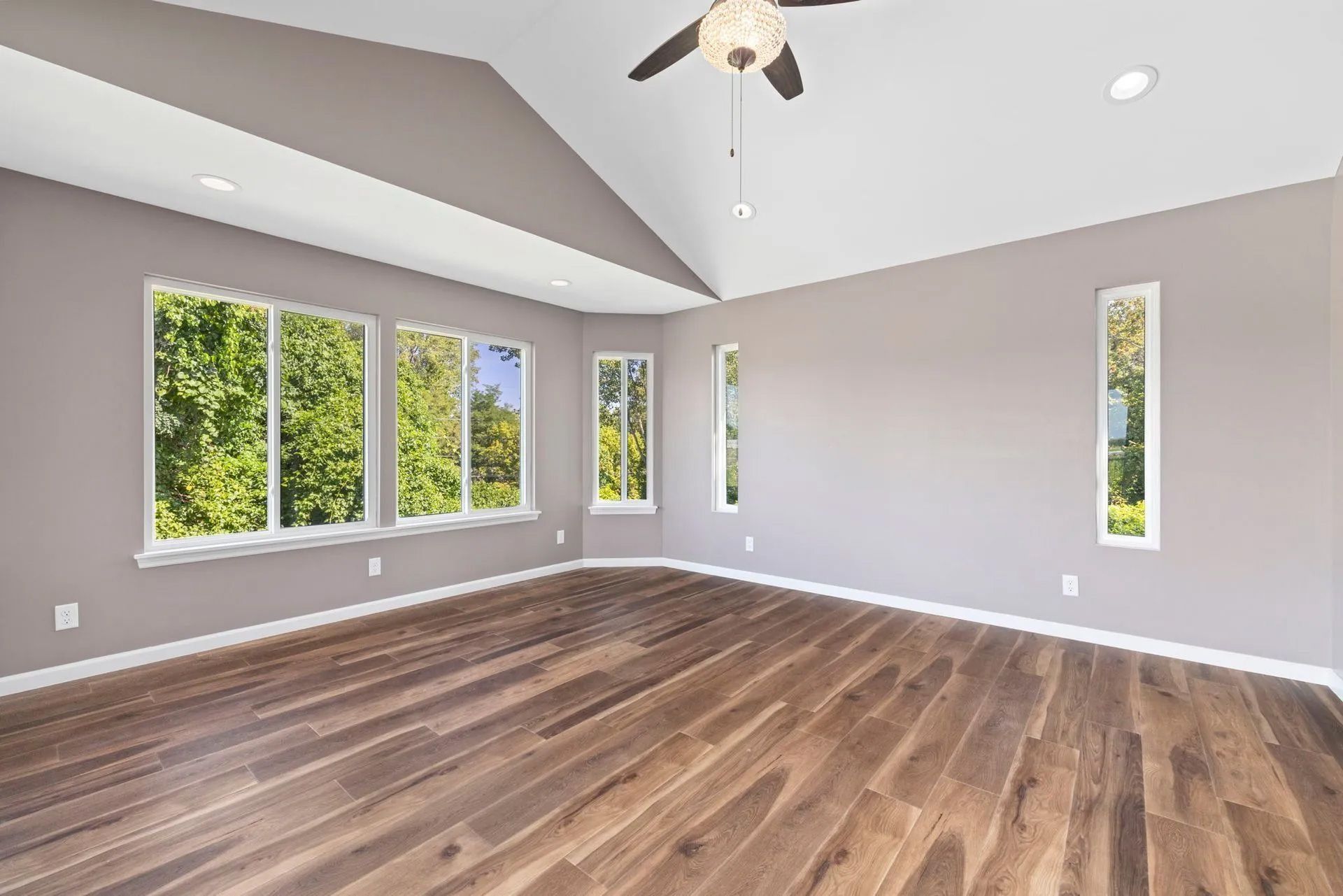 Empty room with hardwood floors, windows, and a high ceiling.