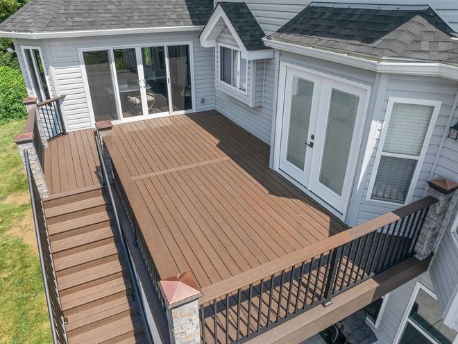 Elevated wooden deck with black railings and two sets of glass doors, attached to a house with gray siding.