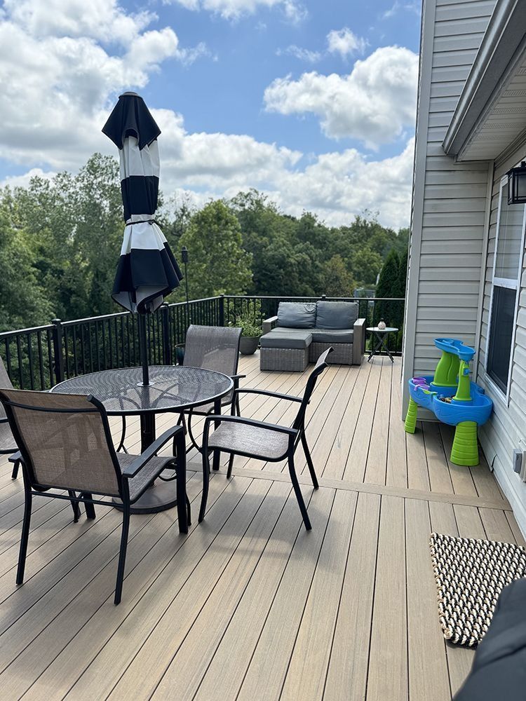 A deck with outdoor furniture, including a table, chairs, and a couch, overlooking a treeline under a cloudy sky.