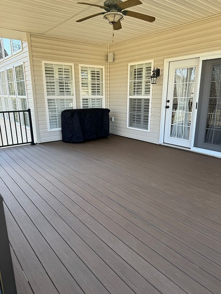 Covered wooden deck with a grill covered in black, and white doors and windows.