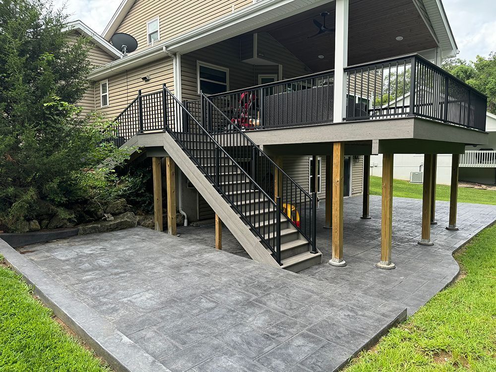 Backyard with elevated deck, stairs, stamped concrete patio, and support pillars.